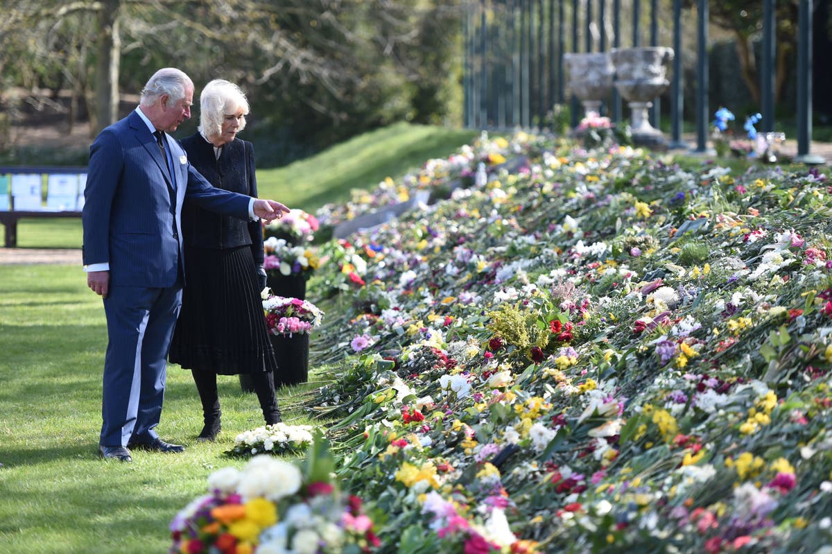 Sombre Prince Charles and Camilla pictured looking at flowers left by public in memory of Prince Philip