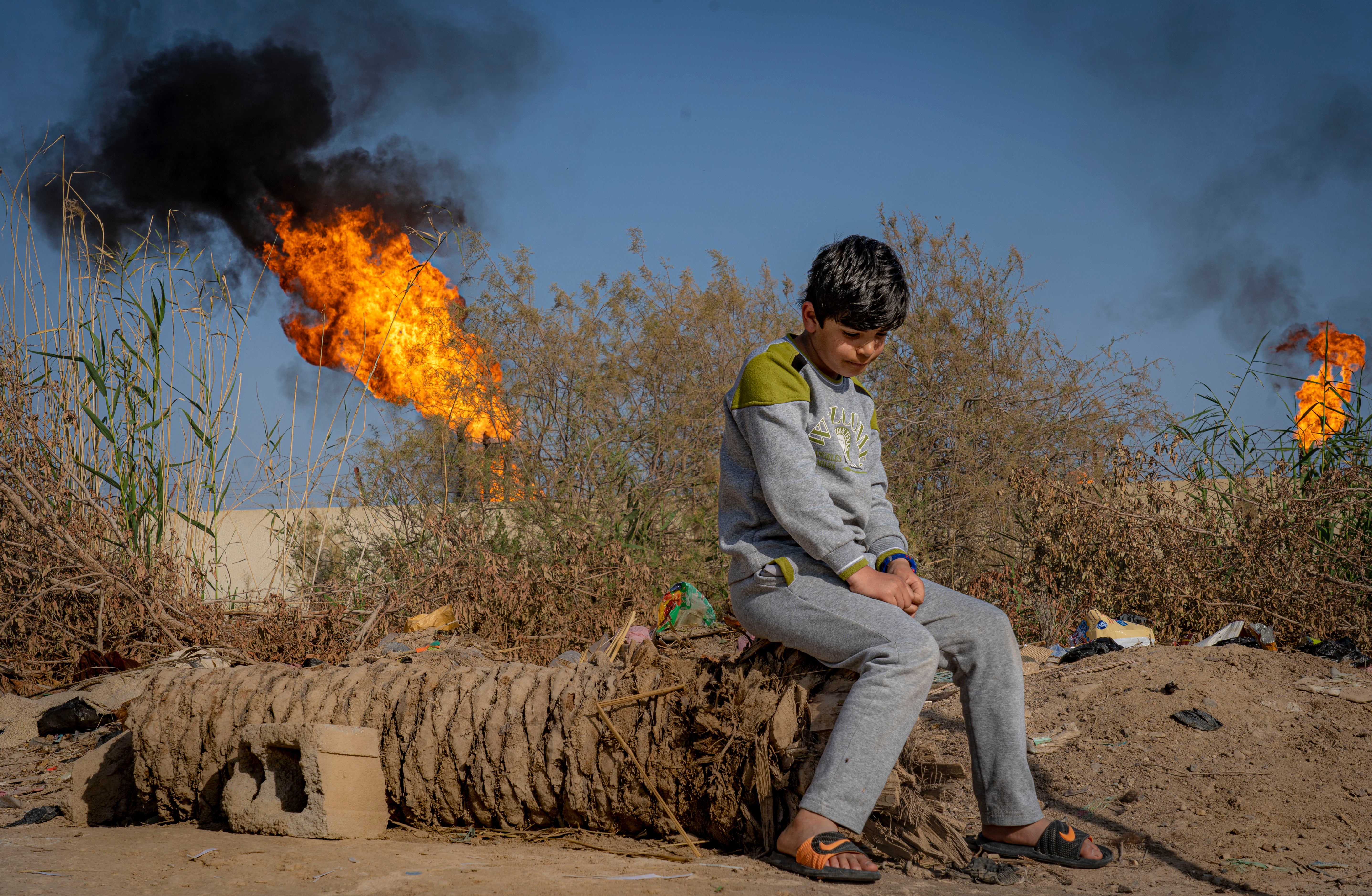 A young boy sits in front of the toxic chimneys of a gas flare in Nahran Omar, southern Iraq