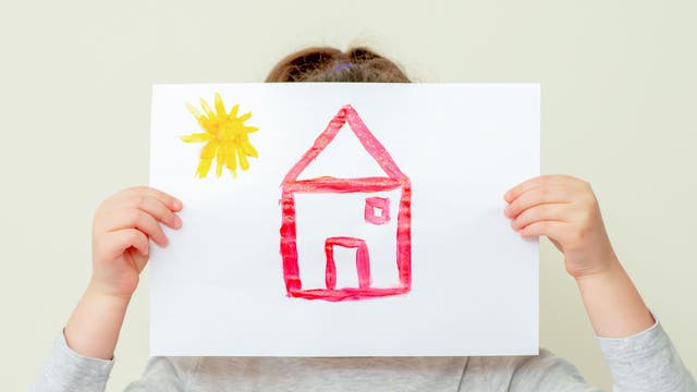 Hands of child holding picture of house covering her face on light background.