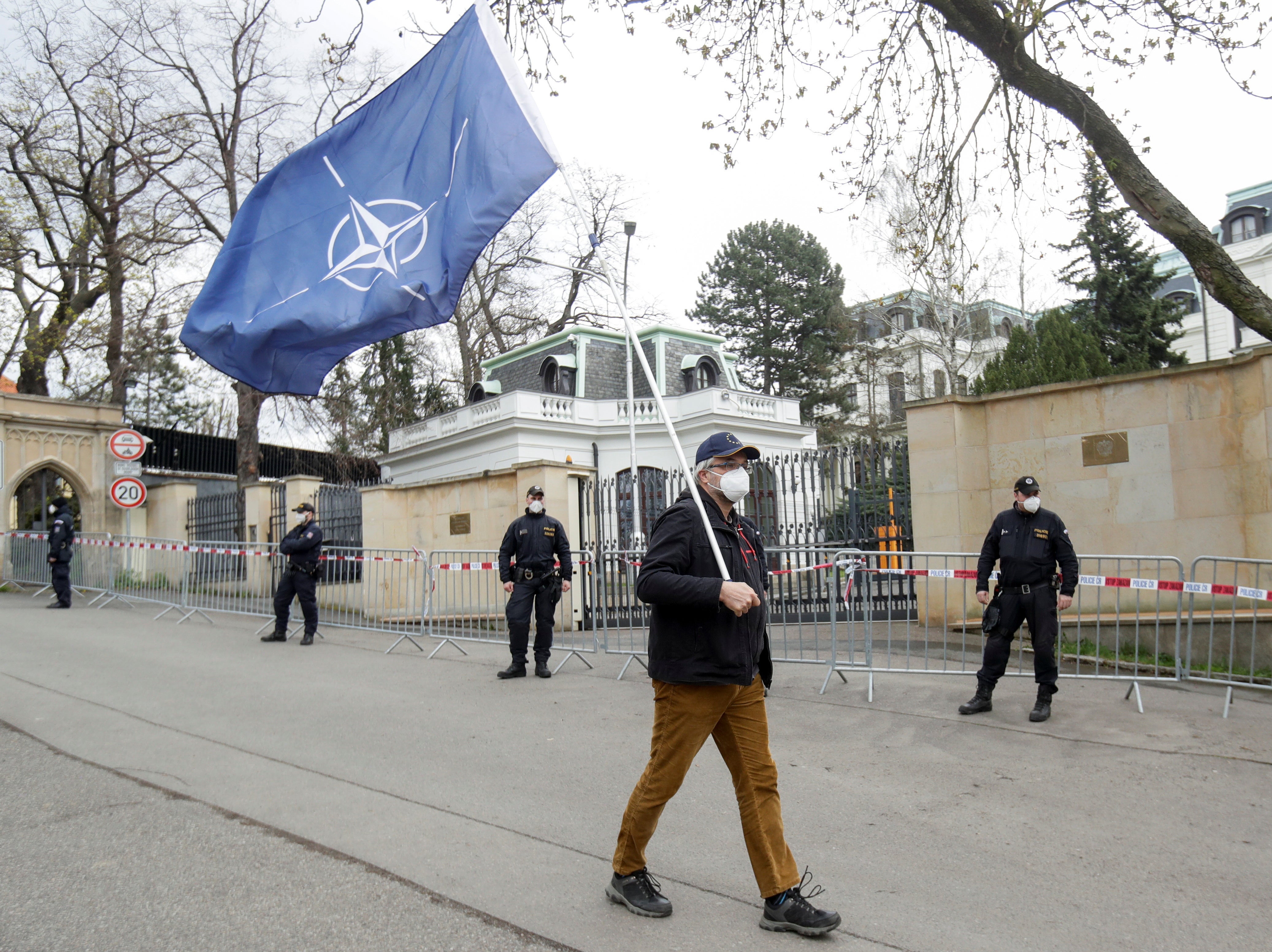 A man carrying a Nato flag to protest over Russian intelligence services’ alleged involvement in an ammunition depot explosion in the Vrbetice area in 2014 walks past police officers outside the Russian embassy in Prague, 18 April 2021