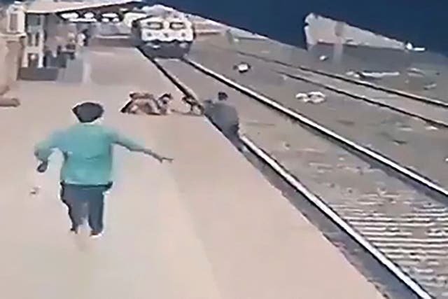 <p>This video frame grab taken from footage released by Indian Ministry of Railways on 20 April, 2021, shows a pointsman (R) saving a child (top C) as he lost his balance and fell in the path of an oncoming train at Vangani railway station in Mumbai</p>