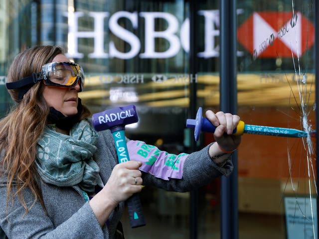 An activist from the Extinction Rebellion shatters a window at HSBC headquarters in Canary Wharf