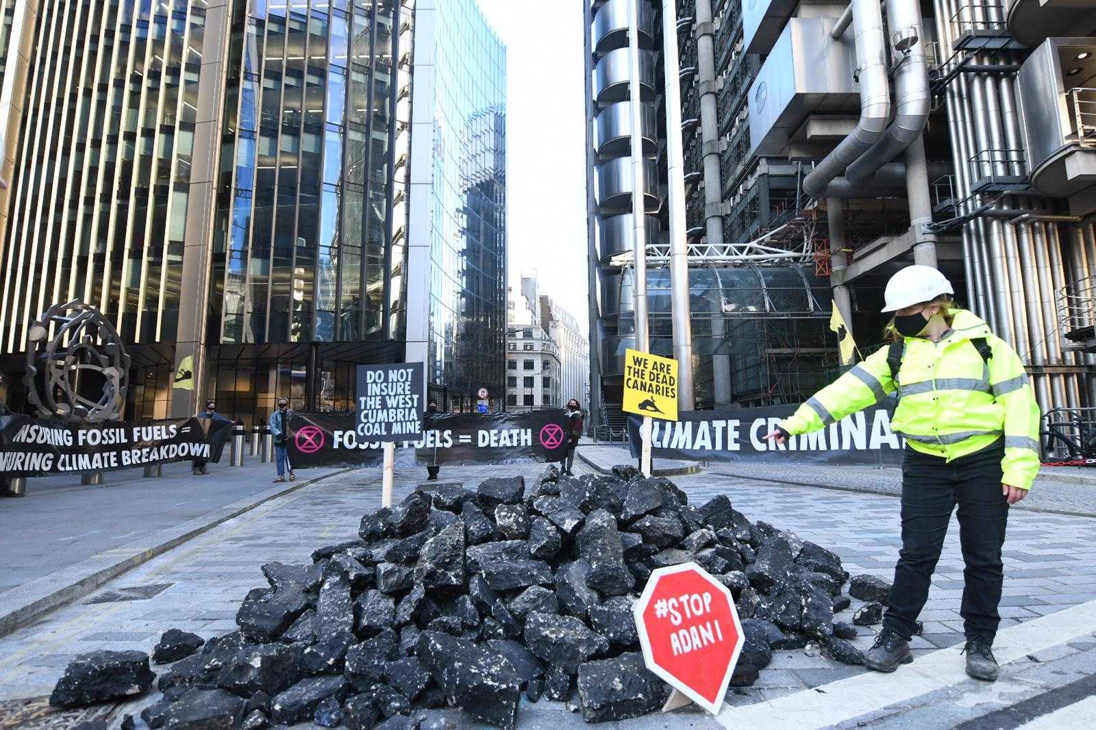 An activist points to a mound of fake coal outside insurance market in central London