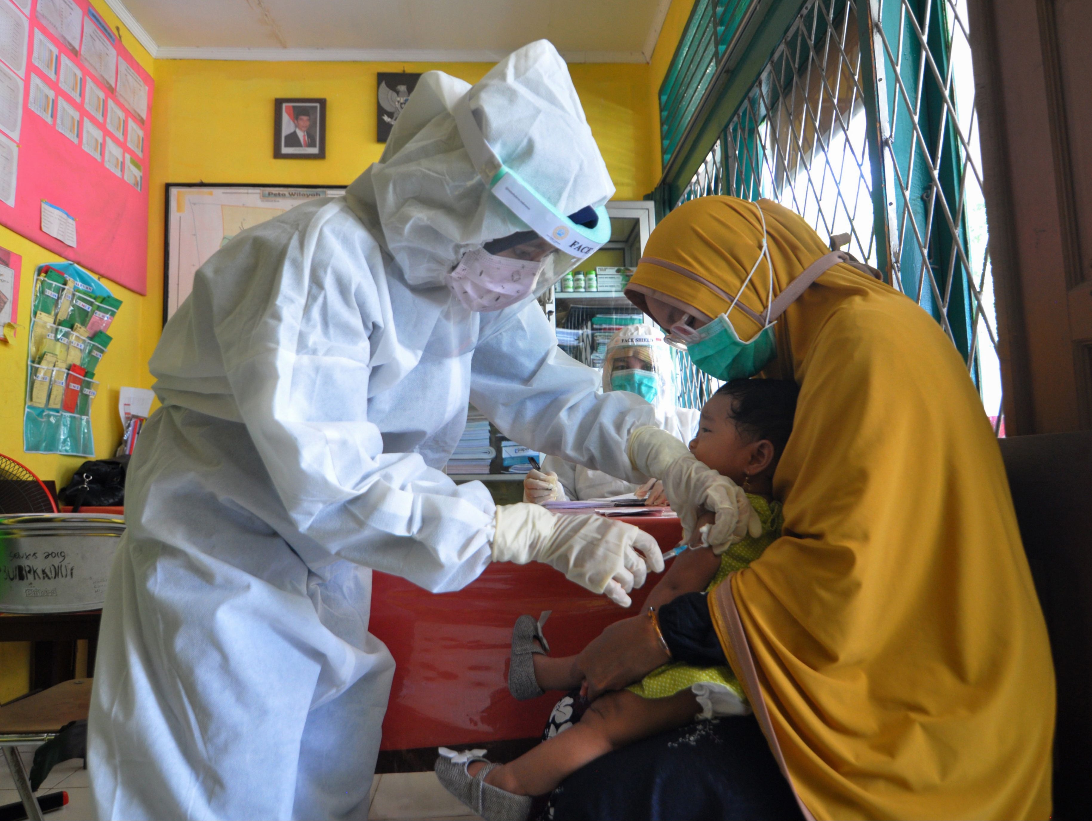 Nurses wearing protective gear administer a vaccine against measles to a child at a health centre in Palu, Indonesia