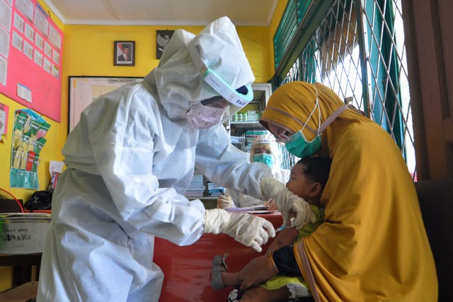 <p>Nurses wearing protective gear administer a vaccine against measles to a child at a health centre in Palu, Indonesia</p>