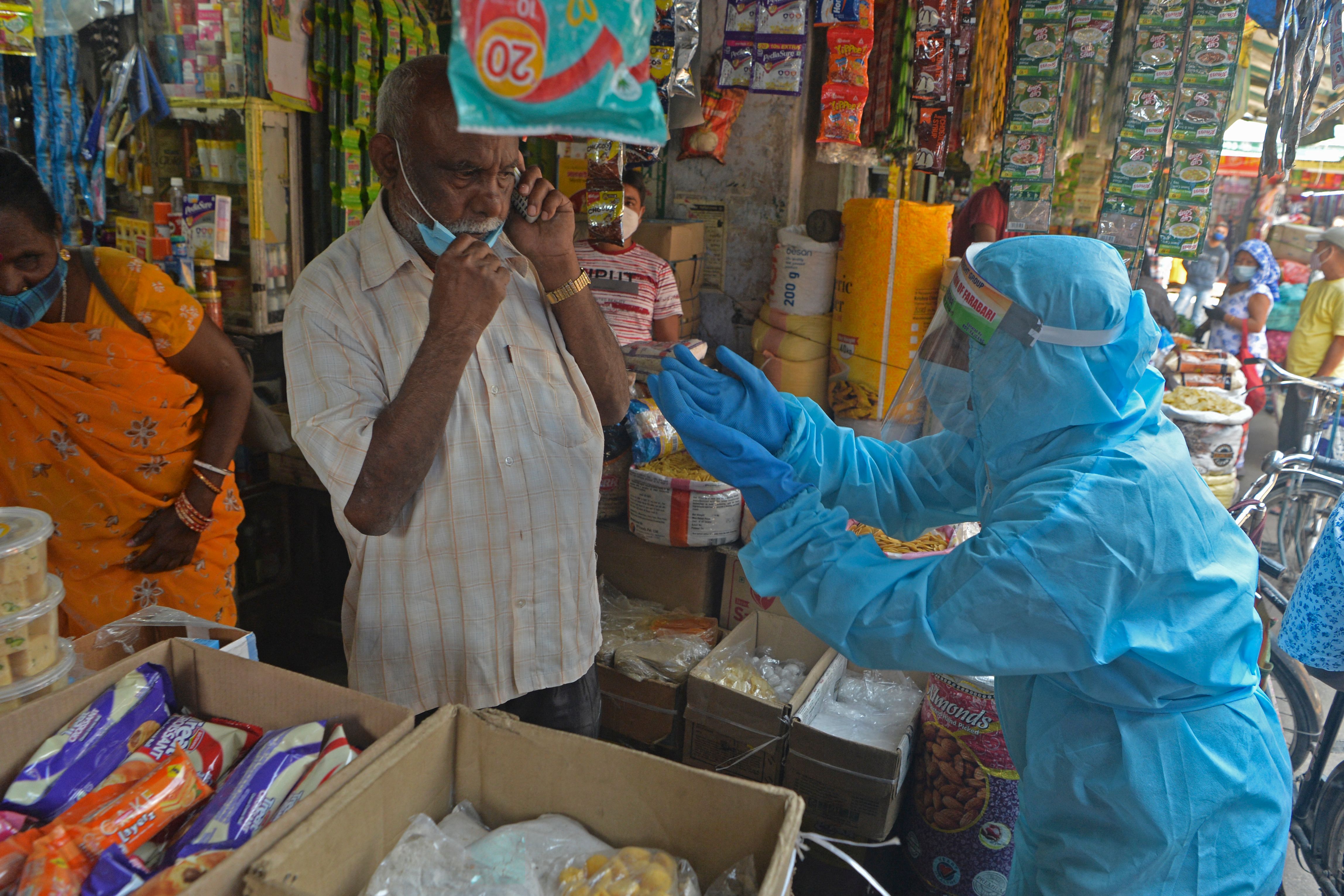 A non-governmental organisation (NGO) volunteer wearing a protective gear urges people in a market to wear facemasks as part of an awareness drive against the spread of the Covid-19 coronavirus in Siliguri on April 23, 2021. (Photo by Diptendu DUTTA / AFP)