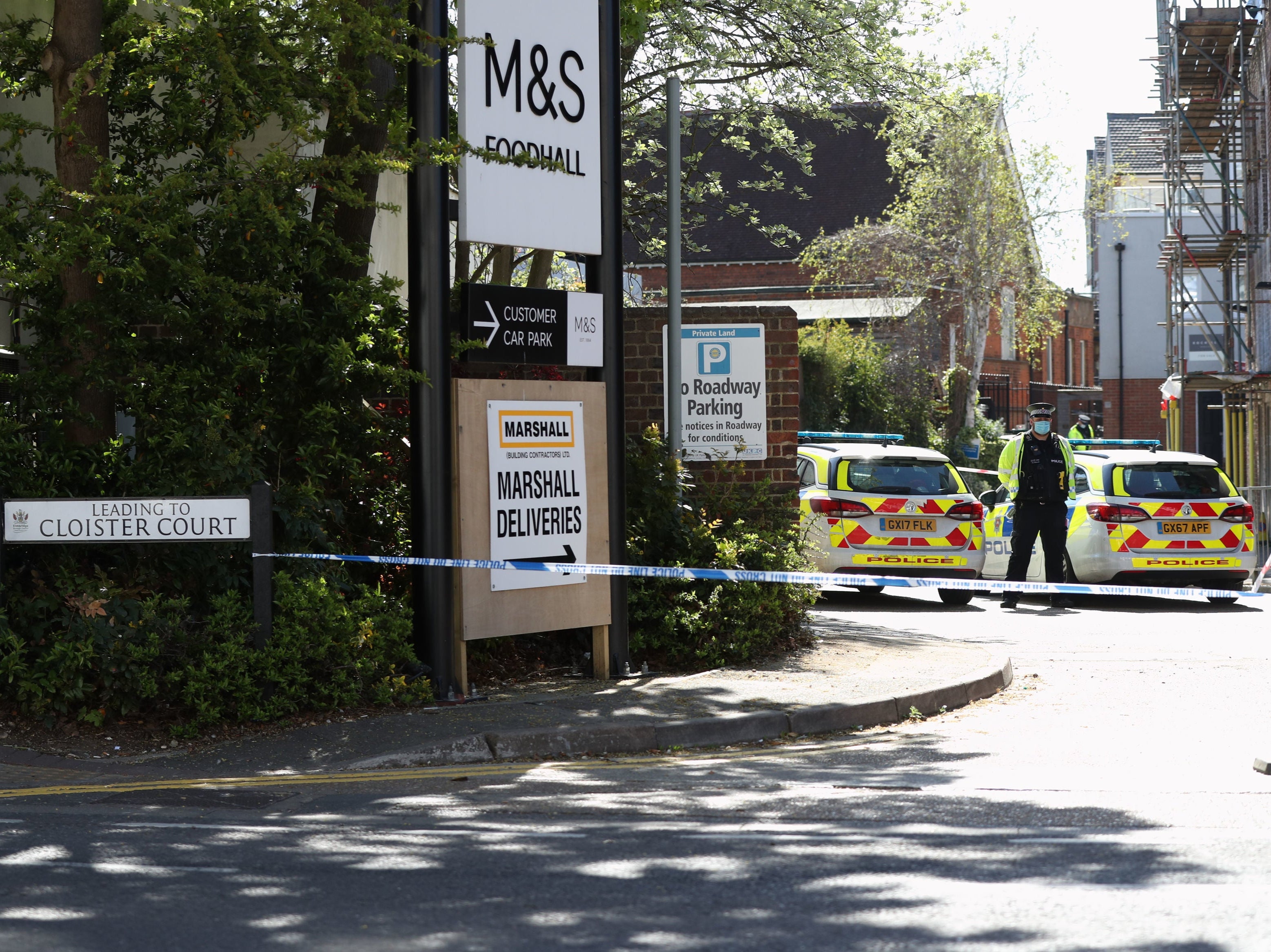 A police officer stands beside a cordon at the junction of Cloister Court and Church Street, Walton-on-Thames, Surrey, where a man died and another was airlifted to hospital after a car was reportedly driven at them