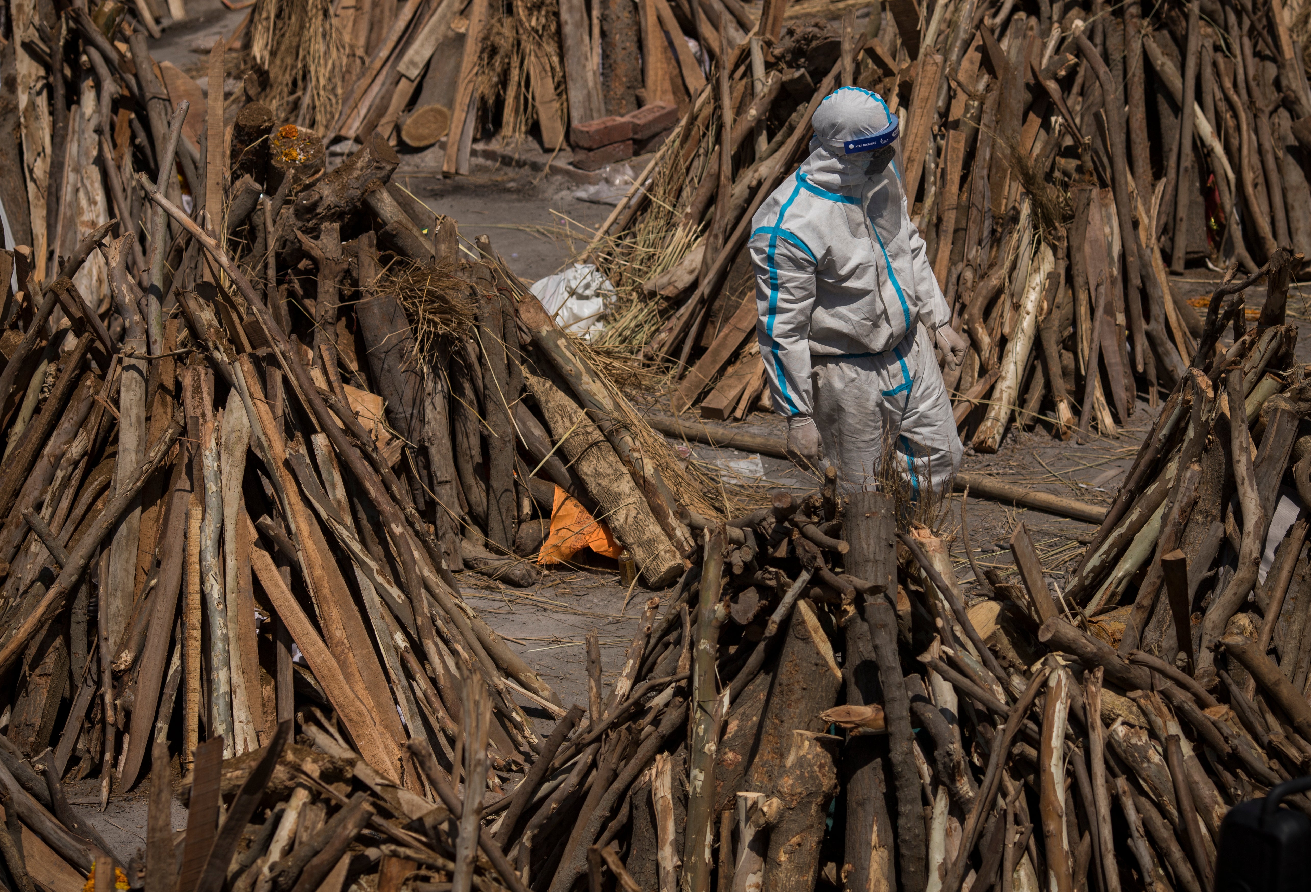 <p>A man wearing PPE walks through funeral pyres at a crematorium in Delhi on Saturday (24 April)</p>