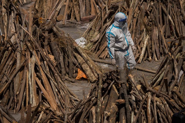 <p>A man wearing PPE walks through funeral pyres at a crematorium in Delhi on Saturday (24 April)</p>