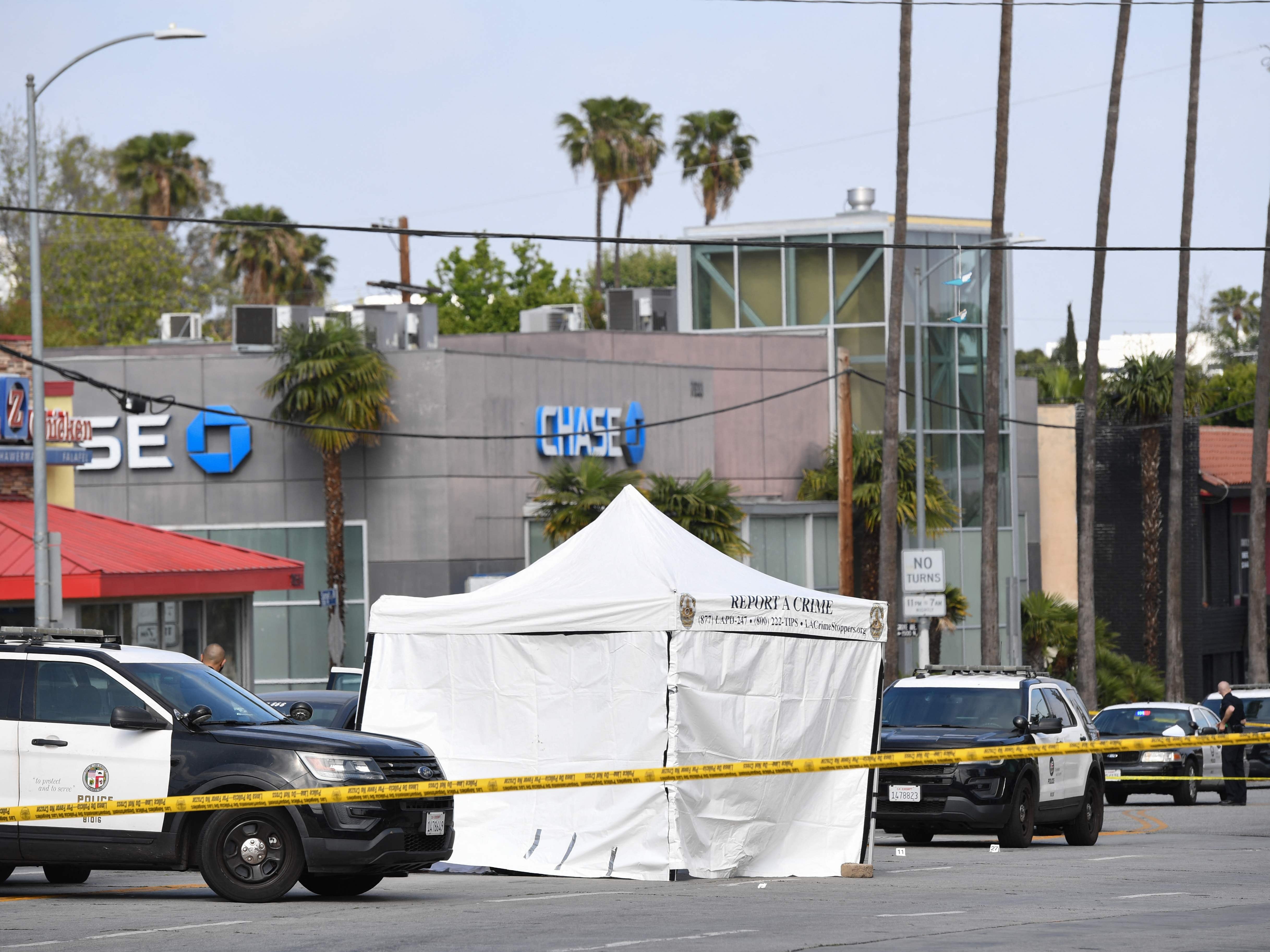 LAPD police cars block the corner of Fairfax Avenue and Sunset Boulevard where a body covered in a white sheet lies under a tent in Los Angeles on 24 April, 2021