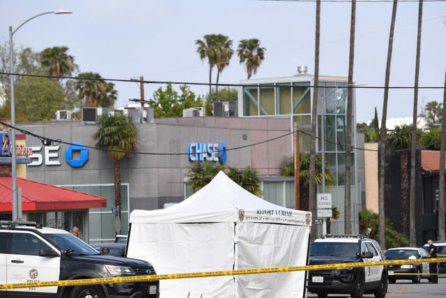 <p>LAPD police cars block the corner of Fairfax Avenue and Sunset Boulevard where a body covered in a white sheet lies under a tent in Los Angeles on 24 April, 2021</p>