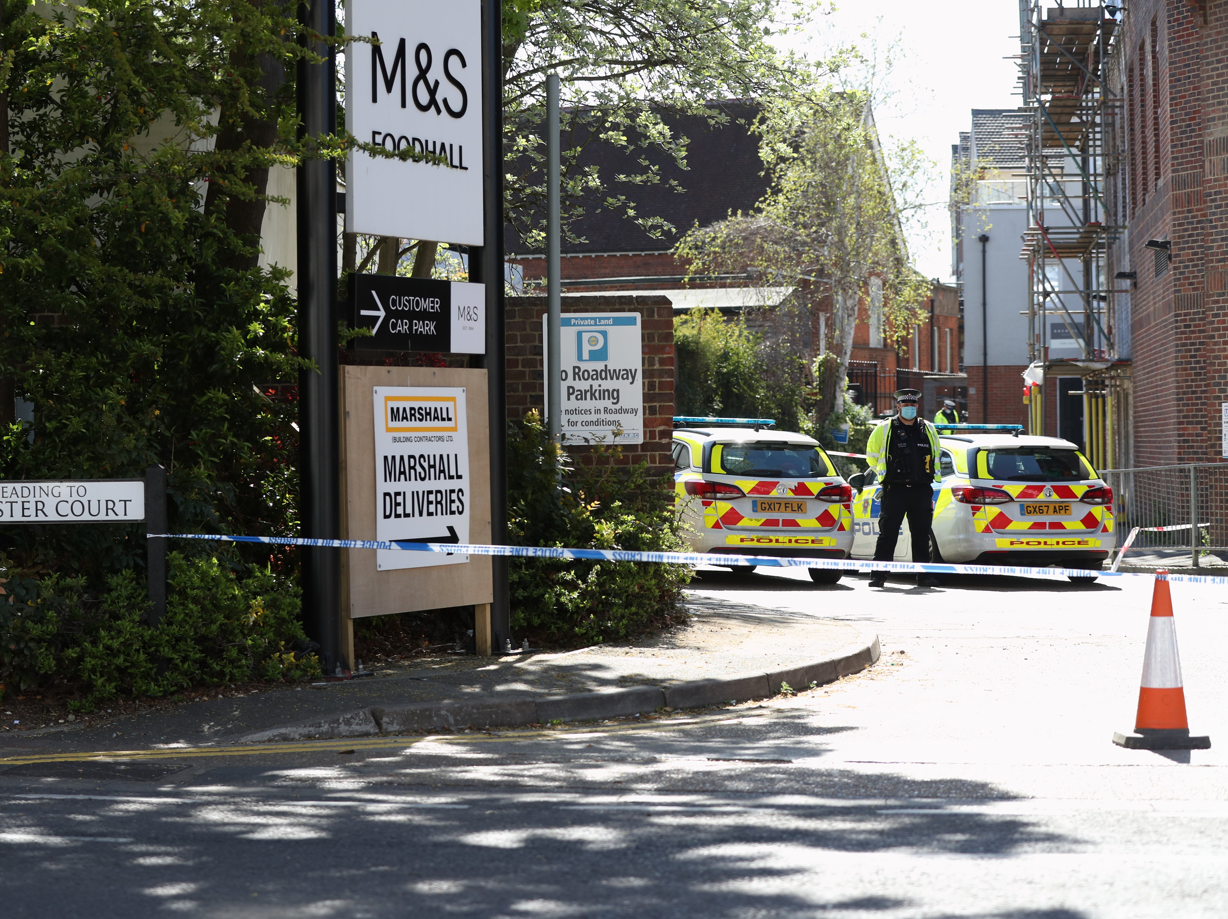 A police officer stands beside a cordon at the junction of Cloister Court and Church Street, Walton-on-Thames, Surrey, where a man died and another was airlifted to hospital after a car was driven at them