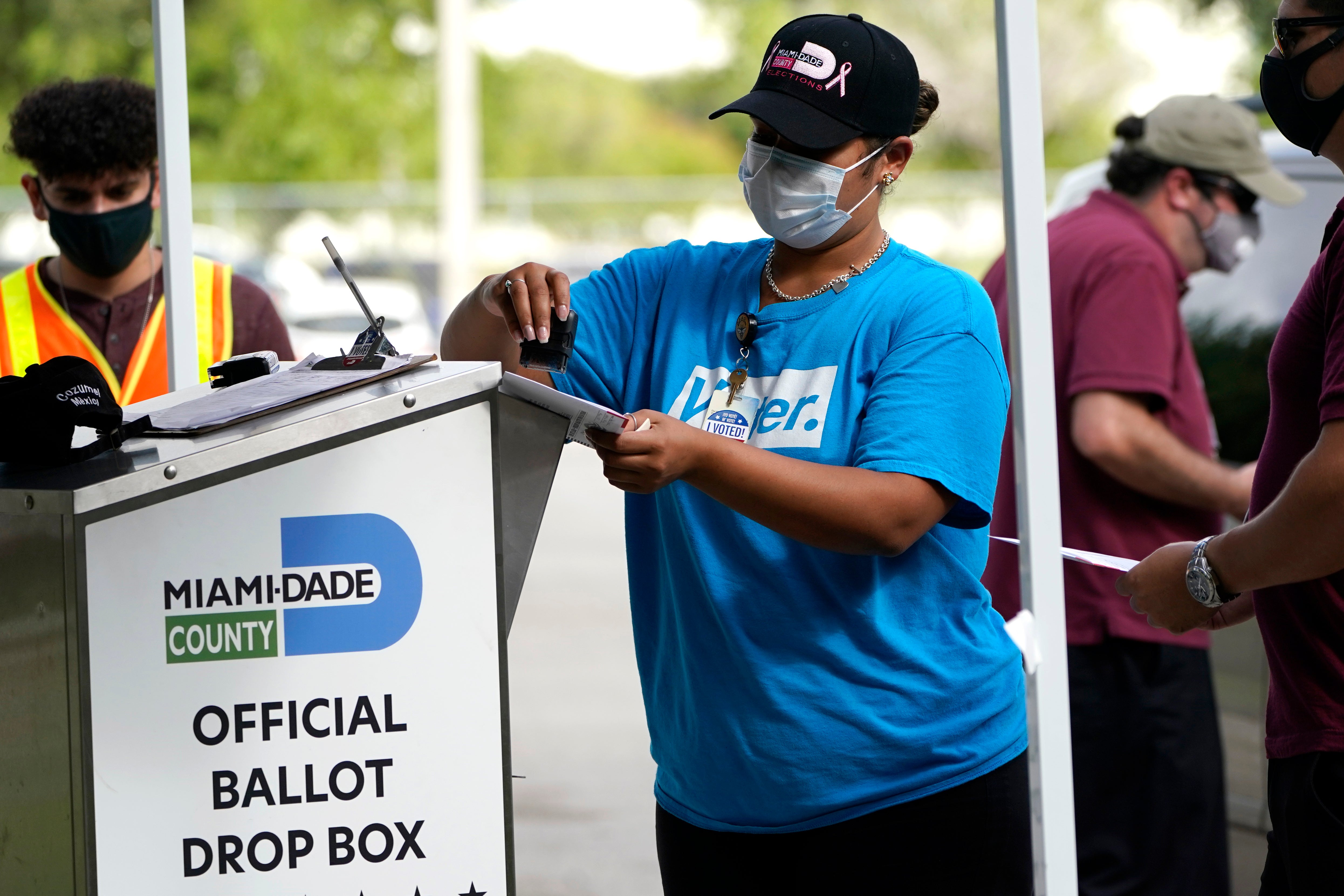 An election worker stamps a vote-by-mail ballot dropped off by a voter before placing it in an official ballot drop box