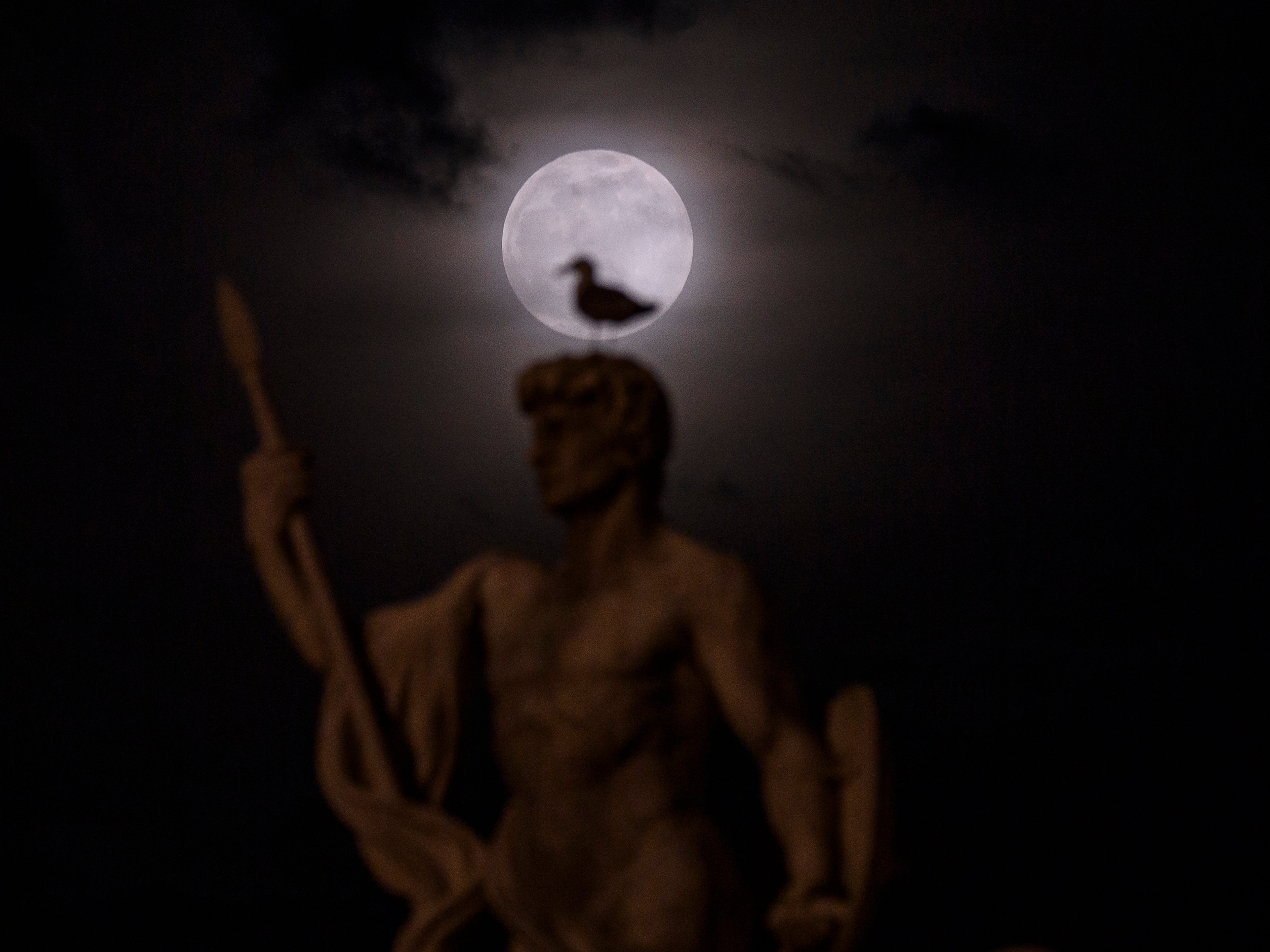 A super moon rises through the clouds behind a statue of the Vittoriano in Rome, Italy