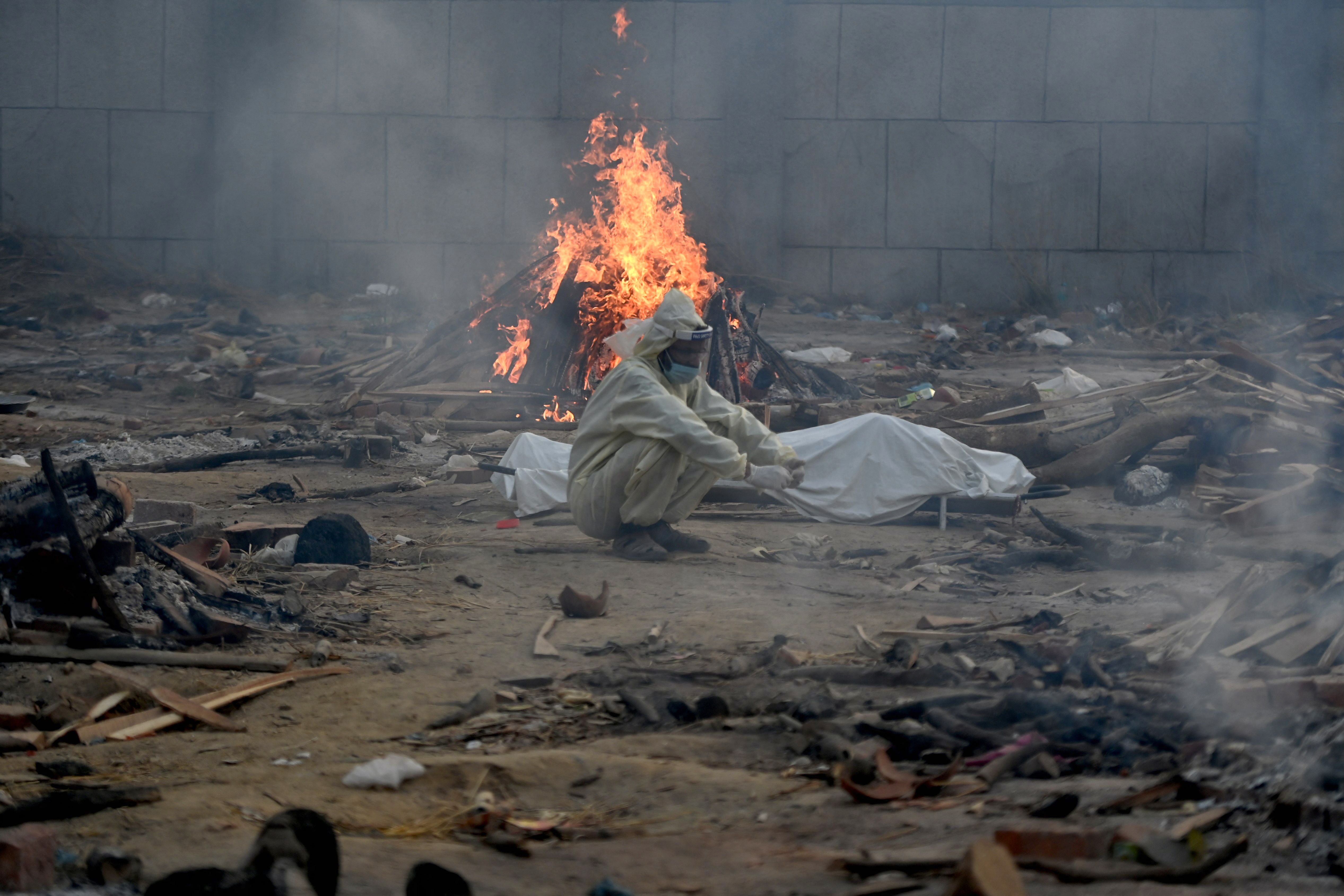 A man sits next to the body of a victim who died of the Covid-19 coronavirus besides the burning pyre of another victim at a cremation ground in New Delhi on April 26, 2021.