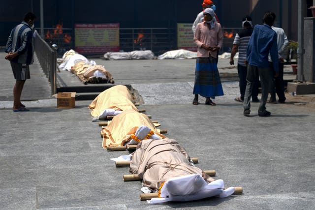 <p>People stand near bodies of Covid-19 coronavirus victims lined up before cremation at a cremation ground in New Delhi on 28 April</p>