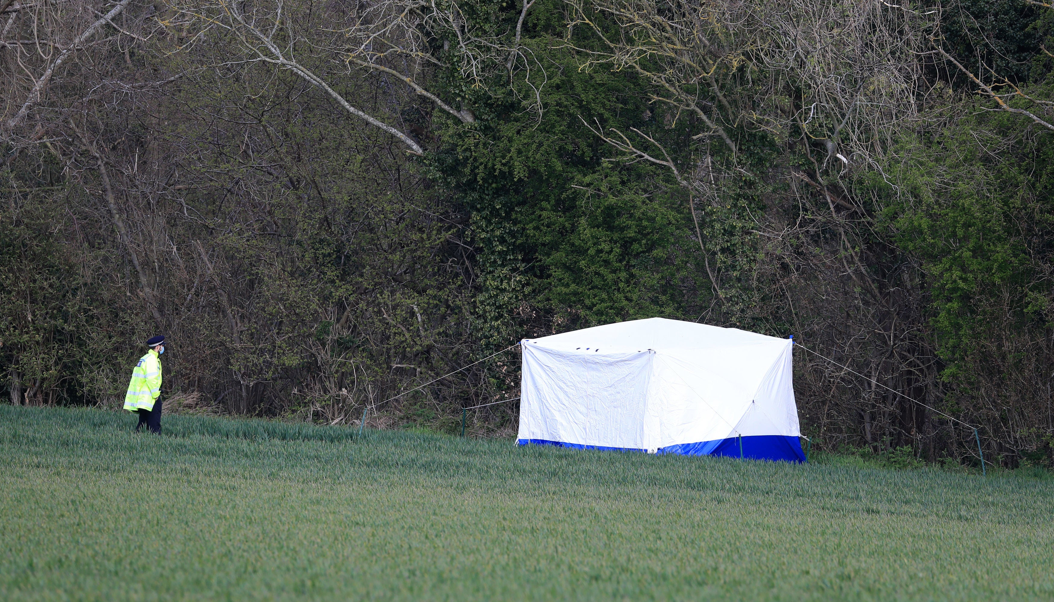 A police officer stands near a forensic tent on the outskirts of Akholt Wood in Snowdown, Kent