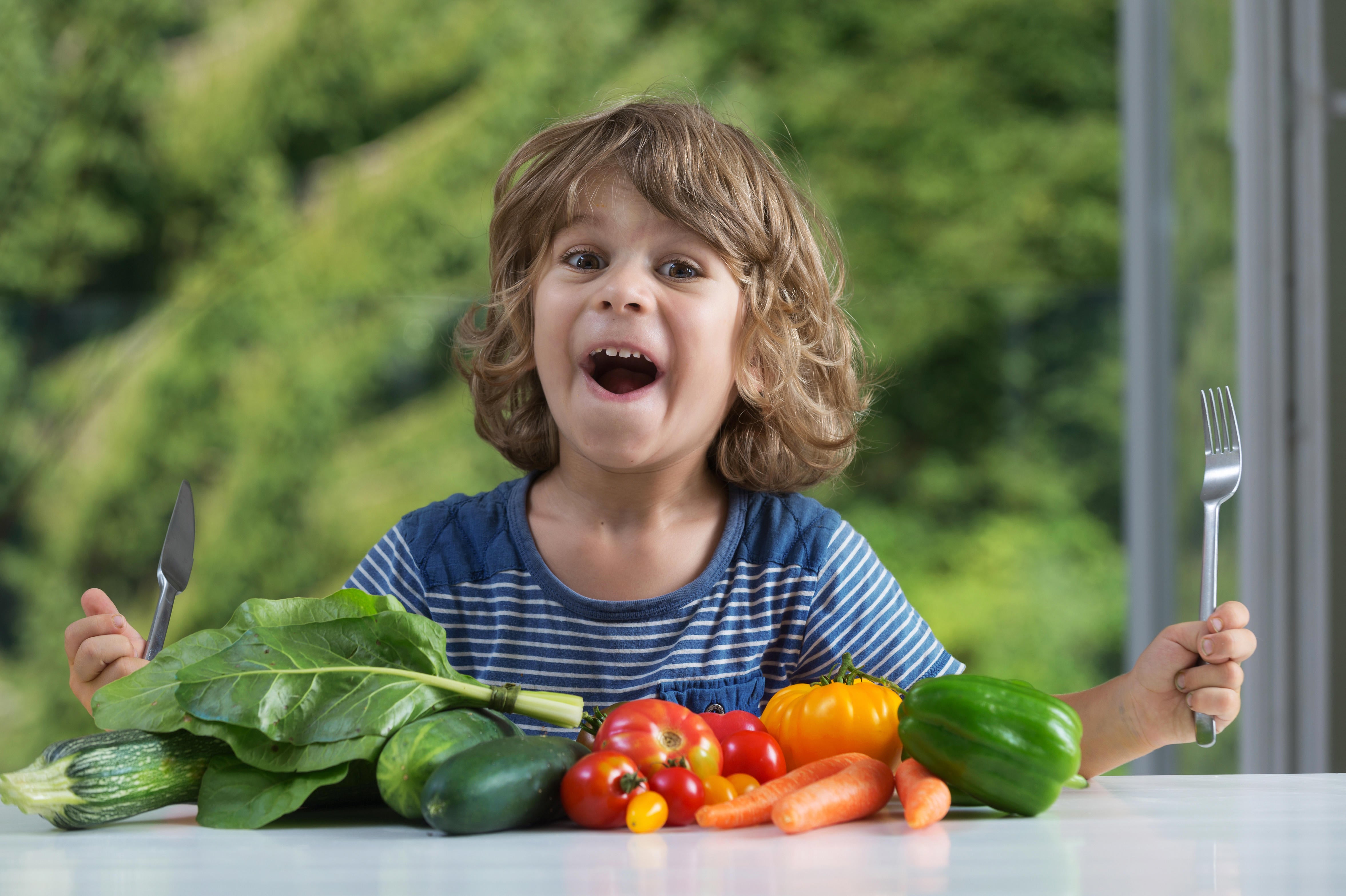 Cute little boy sitting at the table excited about vegetable meal, bad or good eating habits, nutrition and healthy eating, showing emotions concept