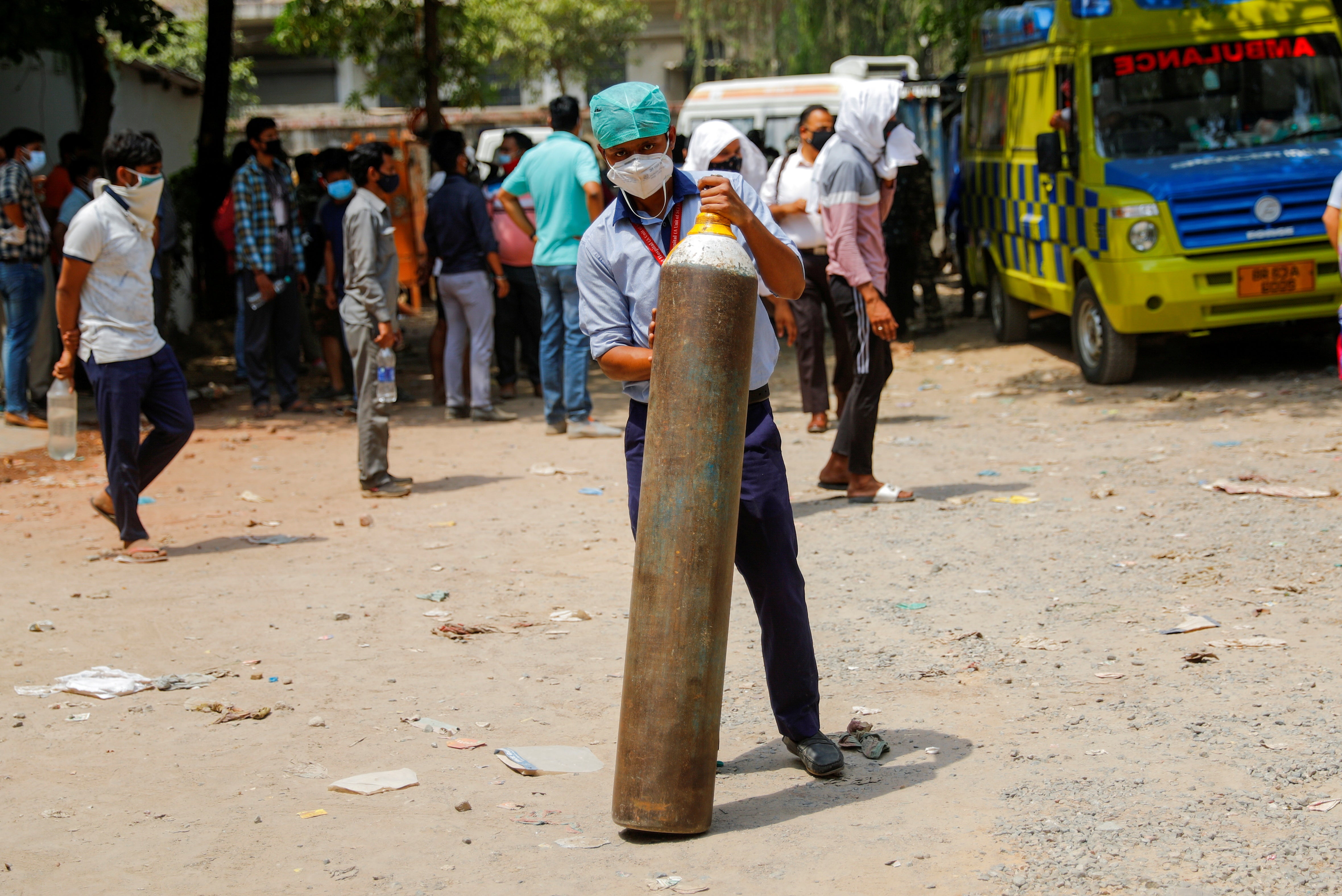 File: A healthcare worker holds an oxygen cylinder outside a factory as he waits to get it refilled
