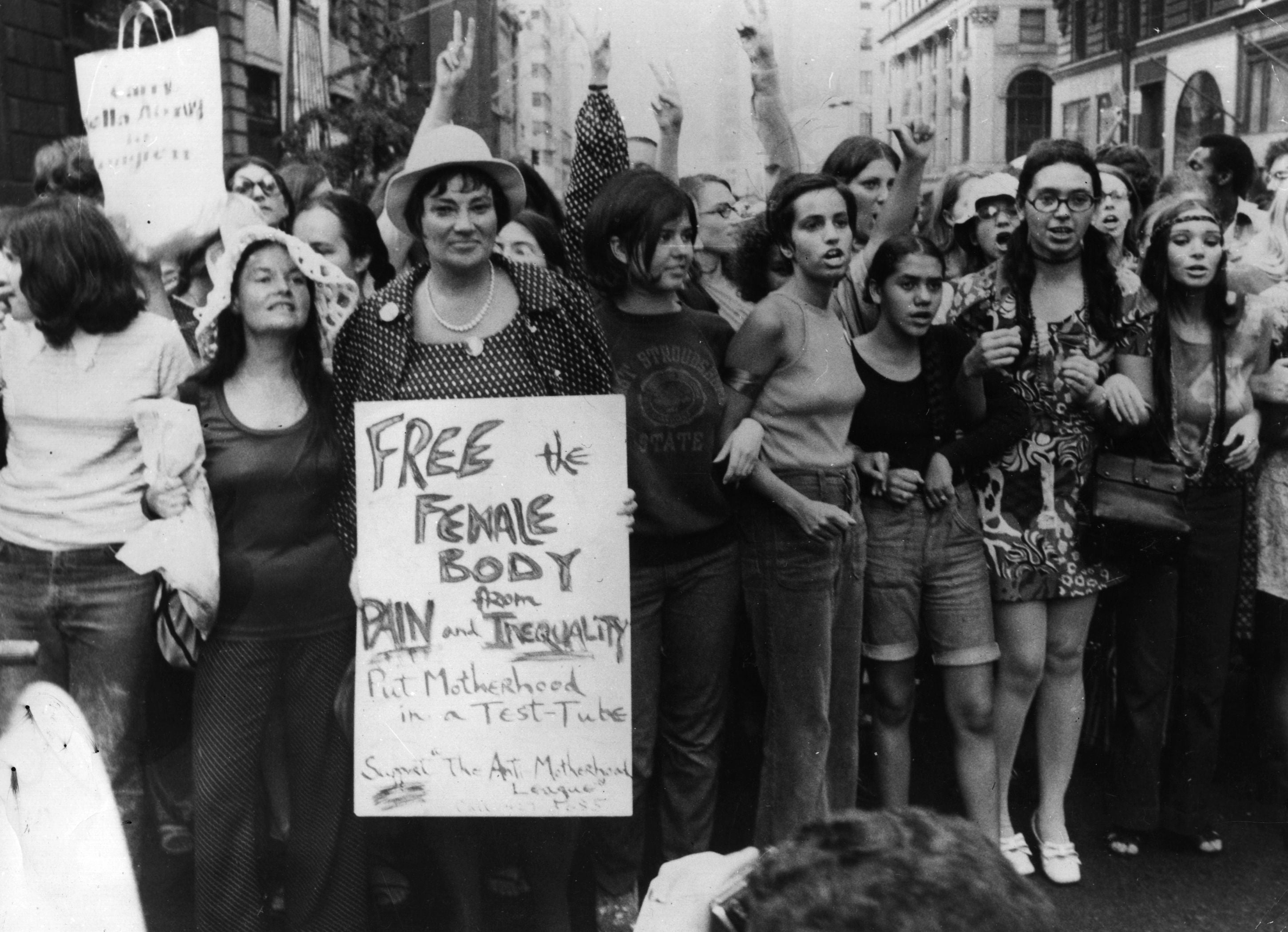 Bella Abzug carries an anti-motherhood sign on the 50th anniversary of women winning the vote in the United States