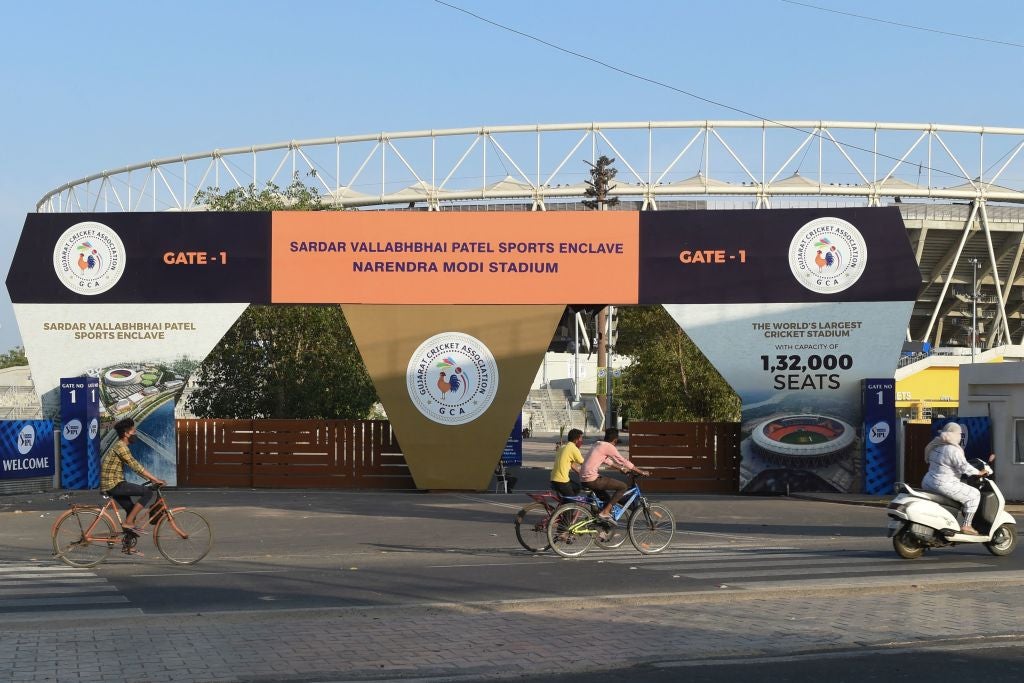 Cyclists cycle past the main entrance of the Narendra Modi Stadium, a venue where cricket matches were taking place during the 2021 Indian Premier League (IPL), in Motera on 4 May 2021 following IPL's decision to suspend the tournament for safety reasons as India battled a massive surge in coronavirus cases
