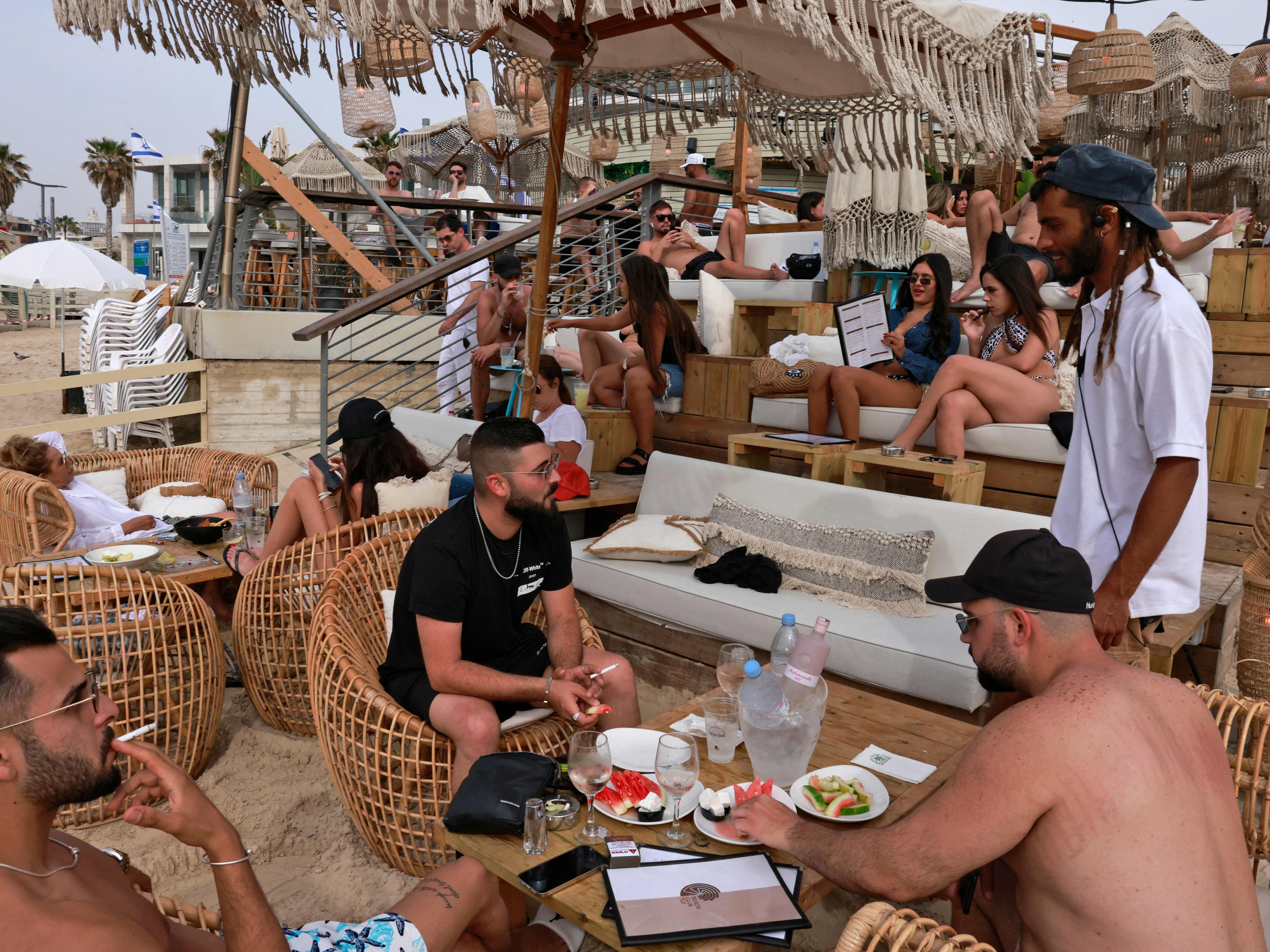 People relax at a beach bar in the Israeli coastal city of Tel Aviv on 19 April after authorities announced face masks were no longer needed outside