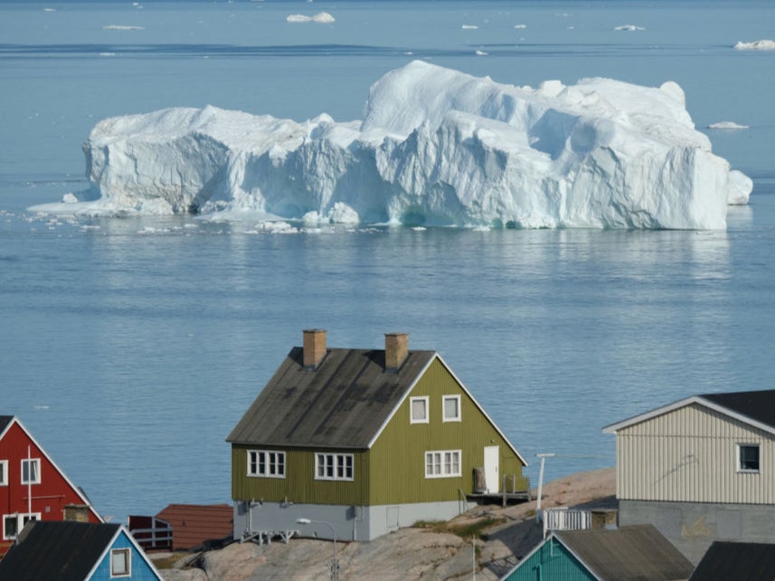 An iceberg floats in Disko Bay behind houses during unseasonably warm weather on July 30, 2019 in Ilulissat, Greenland