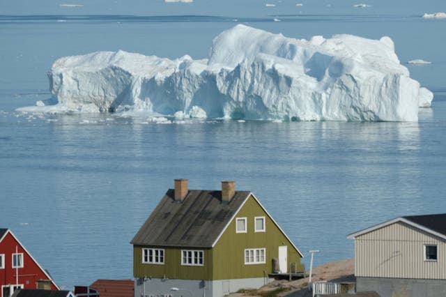 <p> An iceberg floats in Disko Bay behind houses during unseasonably warm weather on July 30, 2019 in Ilulissat, Greenland</p>