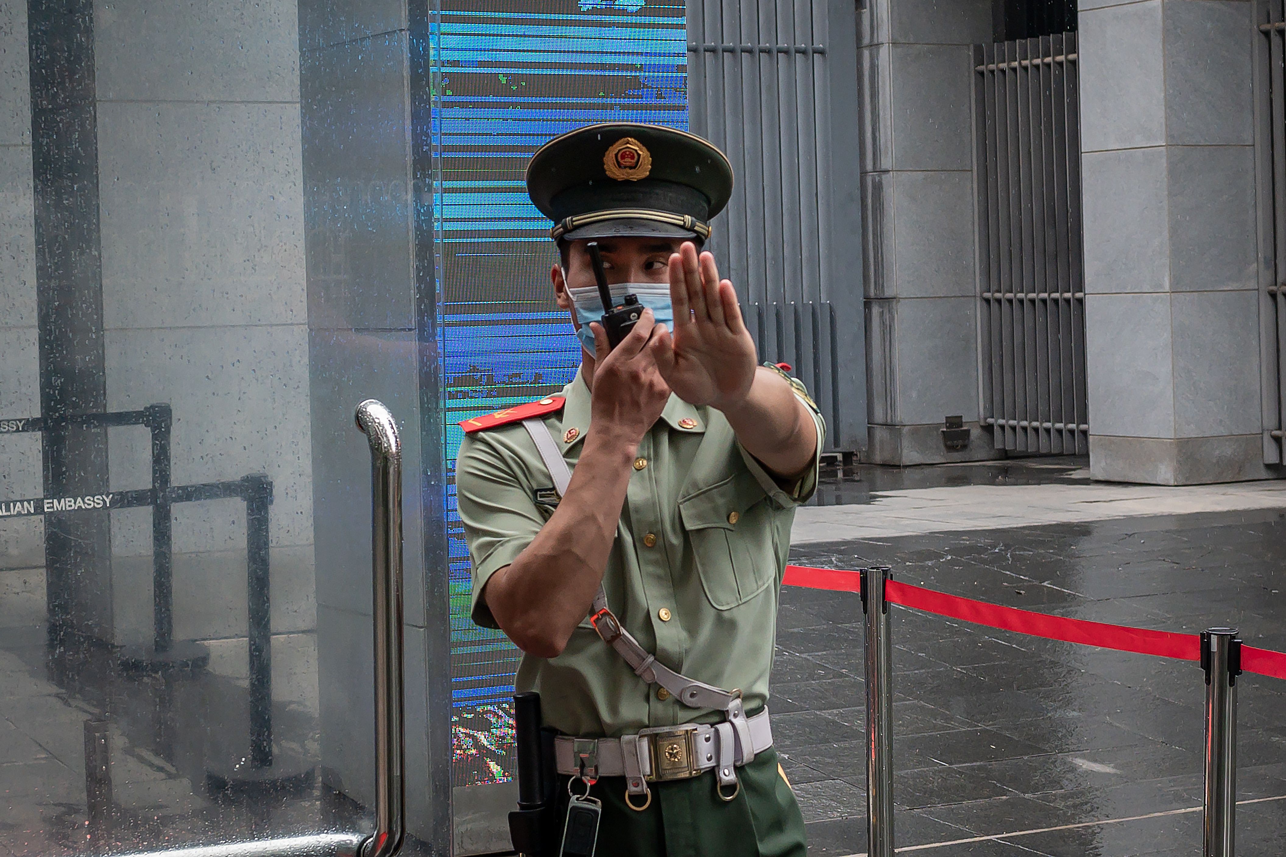 FILE. A Chinese paramilitary police officer gestures and speaks over his two-way radio while standing at the entrance gate of the Australian embassy in Beijing on July 9, 2020. - China has suspended “indefinitely” its key economic dialogue with Australia.