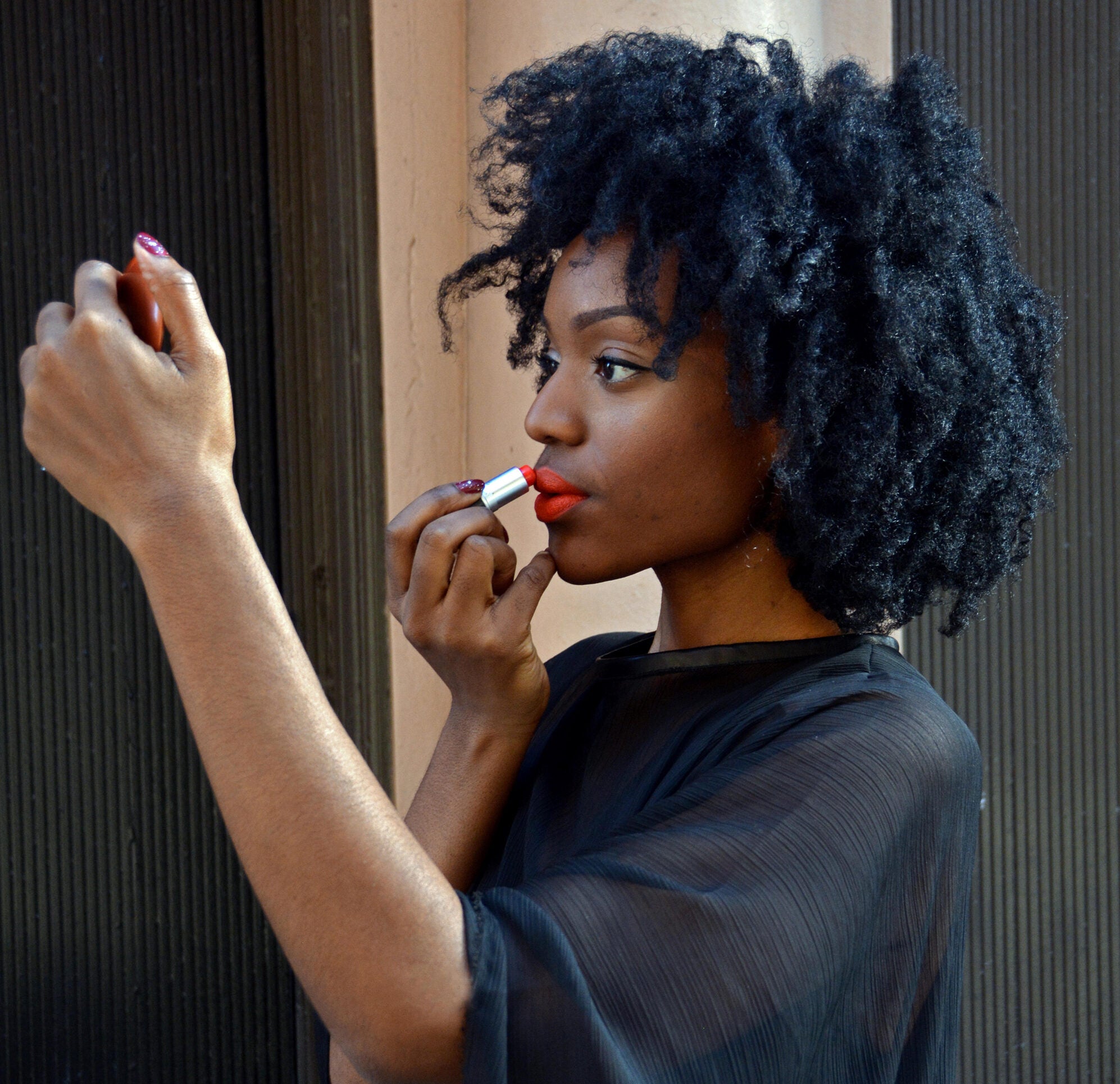 black woman applying red lipstick looking in a hand mirror