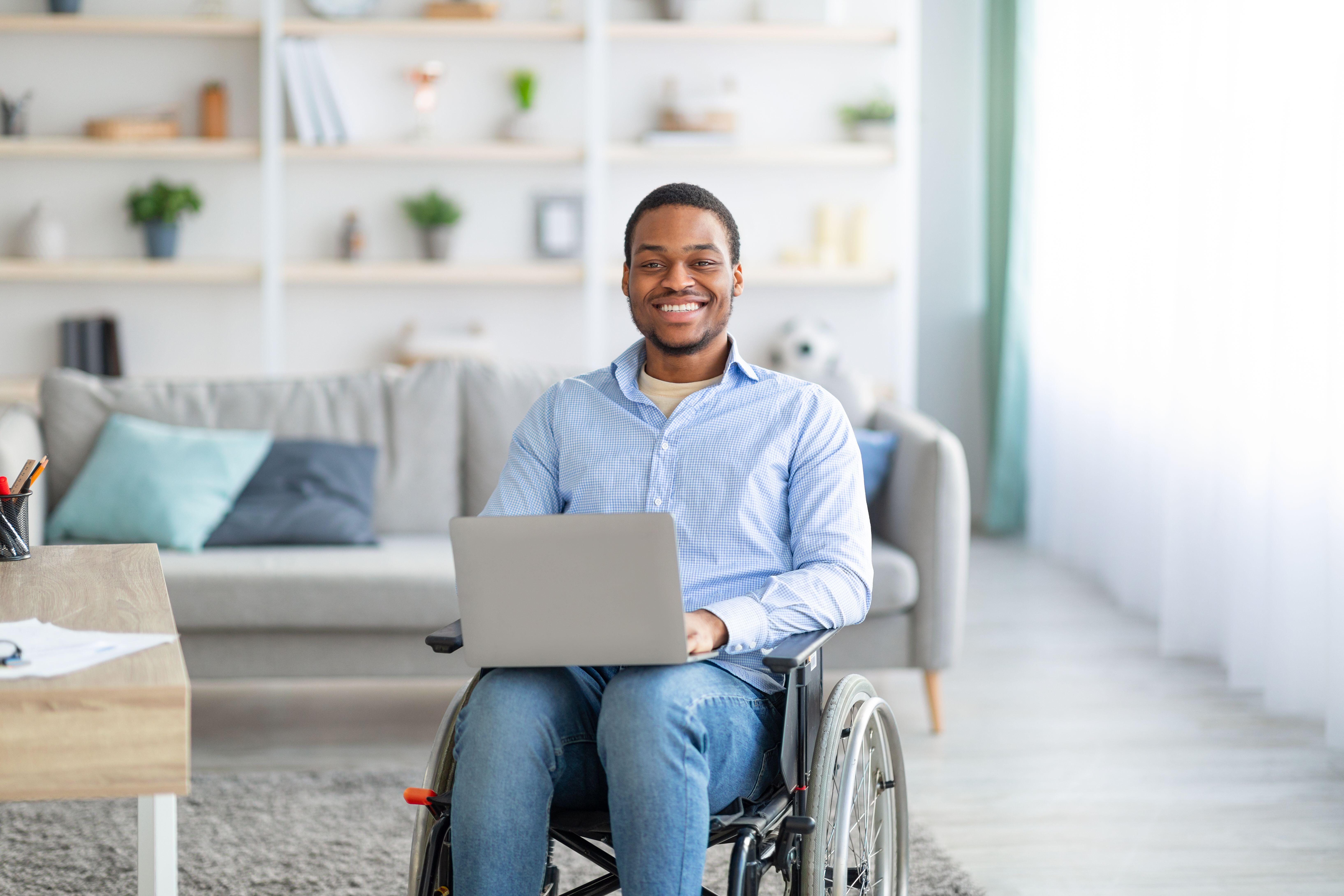 Young black man in wheelchair with laptop, smiling at the camera
