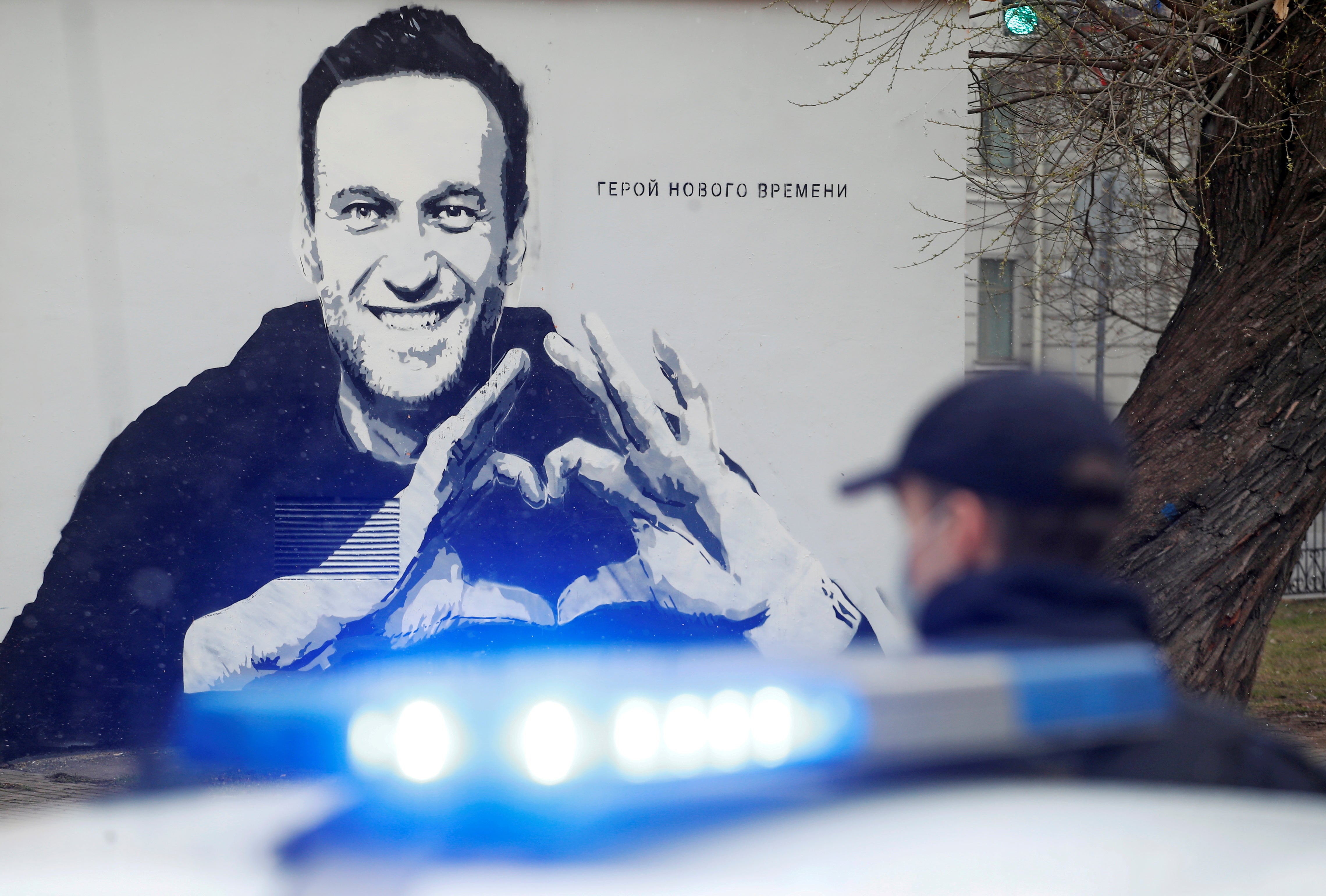 A police officer stands next to a car in front of graffiti depicting Alexei Navalny, with the words ‘The hero of the new age’, in Saint Petersburg