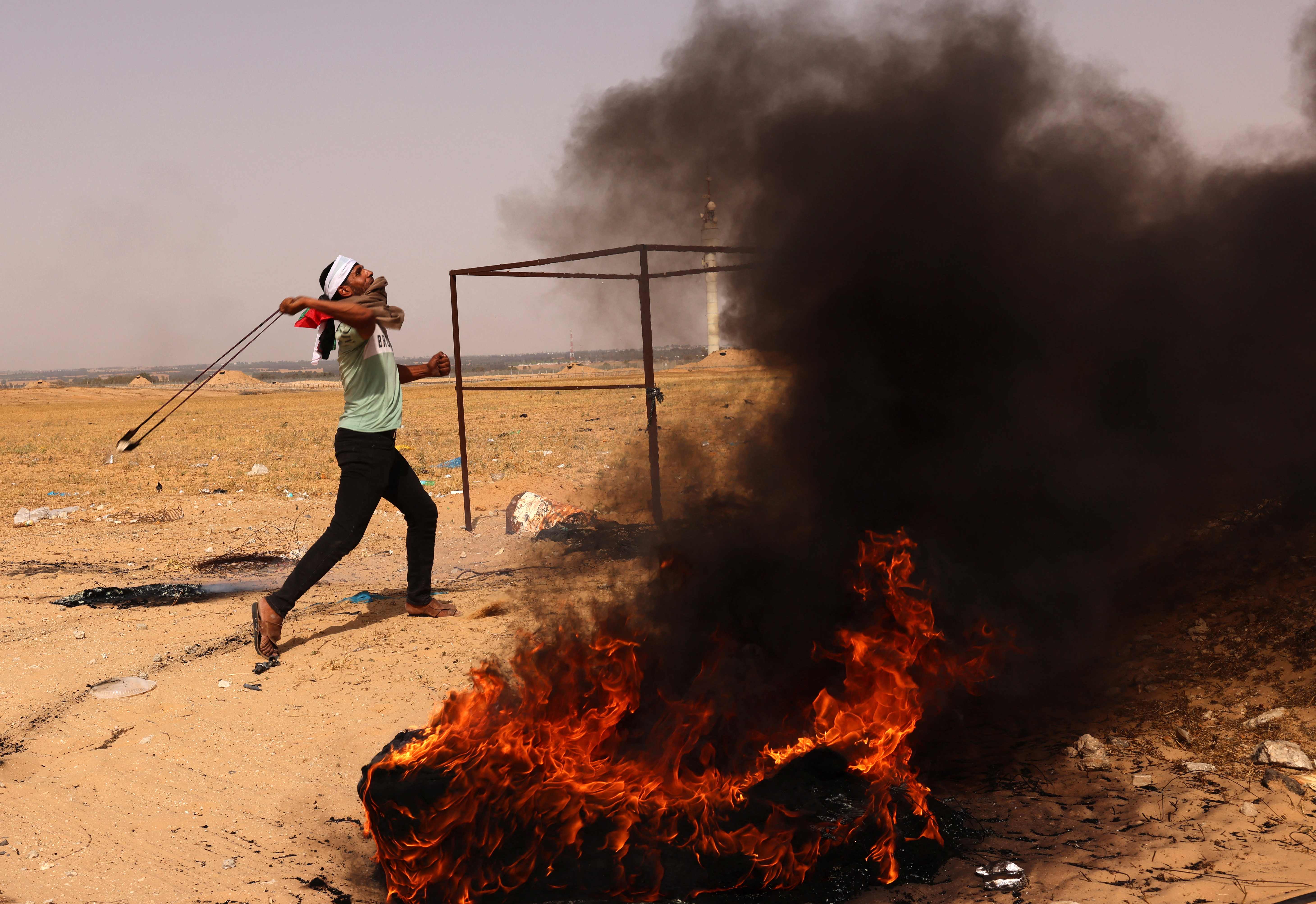 A Palestinian demonstrator hurls rocks next to burning tyres during a protest near to the border with Israel