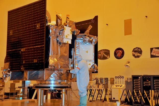The OSIRIS-REx spacecraft sits on its workstand August 20, 2016 while an engineer checks the protective covering in a servicing building at Kennedy Space Center, Florida