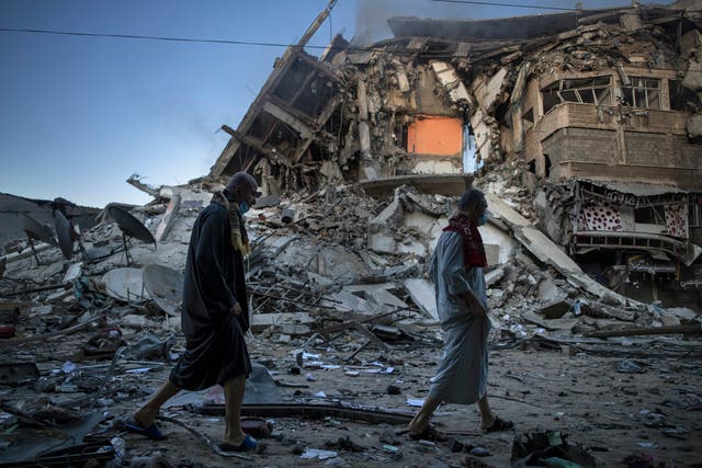 <p>Palestinians walk next to the remains of a destroyed building after Israeli air strikes on Gaza City</p>