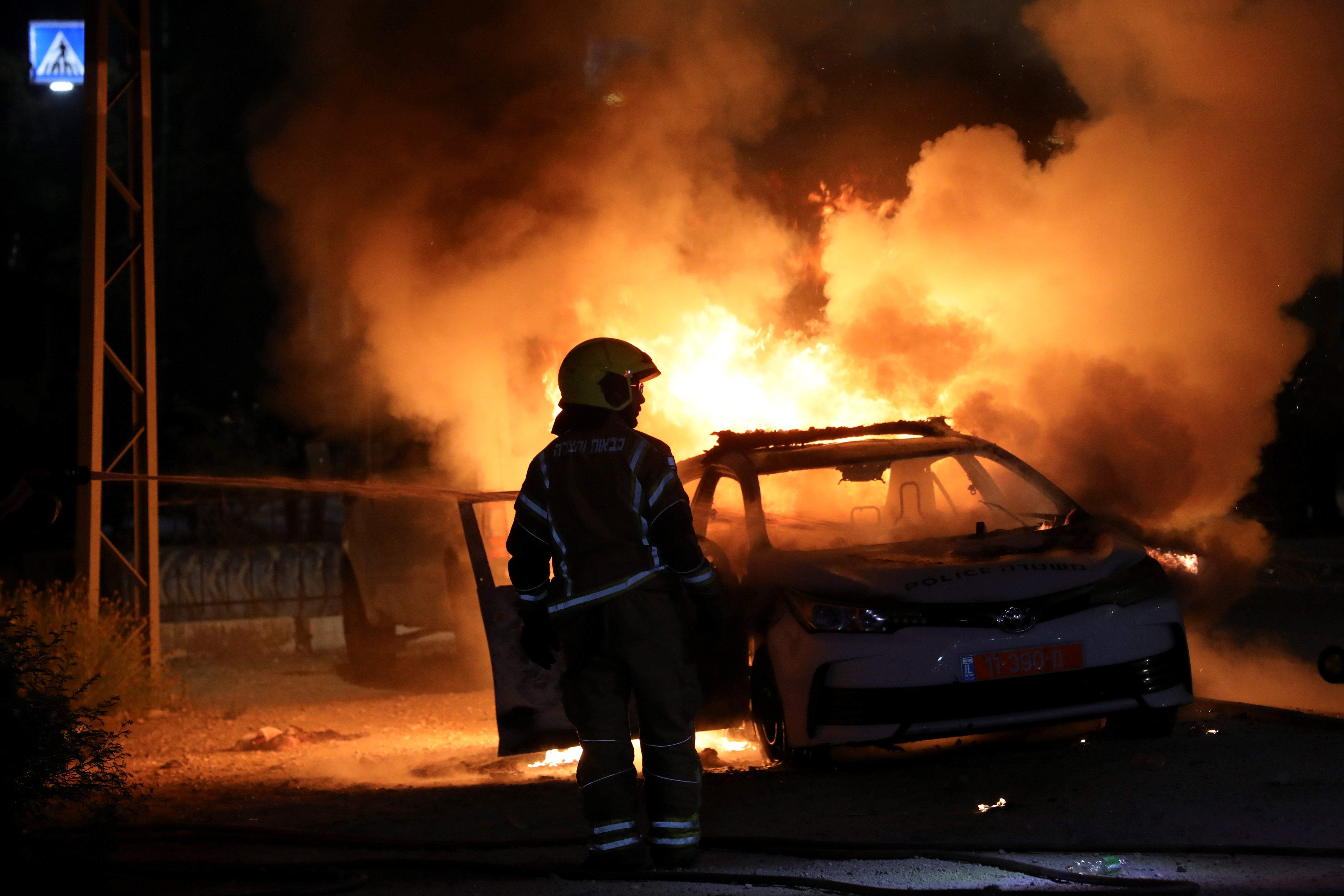 An Israeli firefighter by a burning police car in Lod