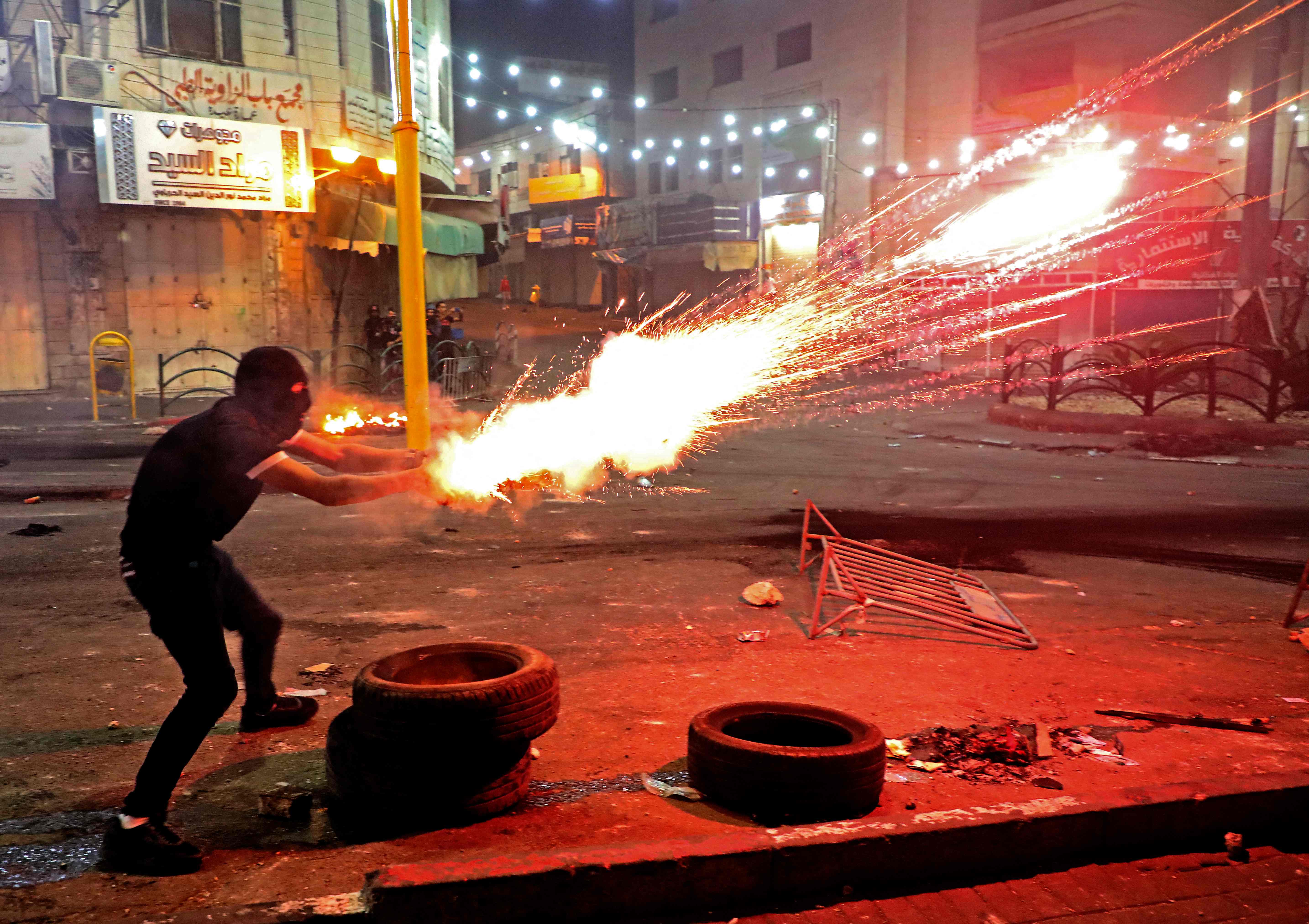 A Palestinian protester launches flares amid clashes with Israeli soldiers in the city centre of Hebron in the West Bank