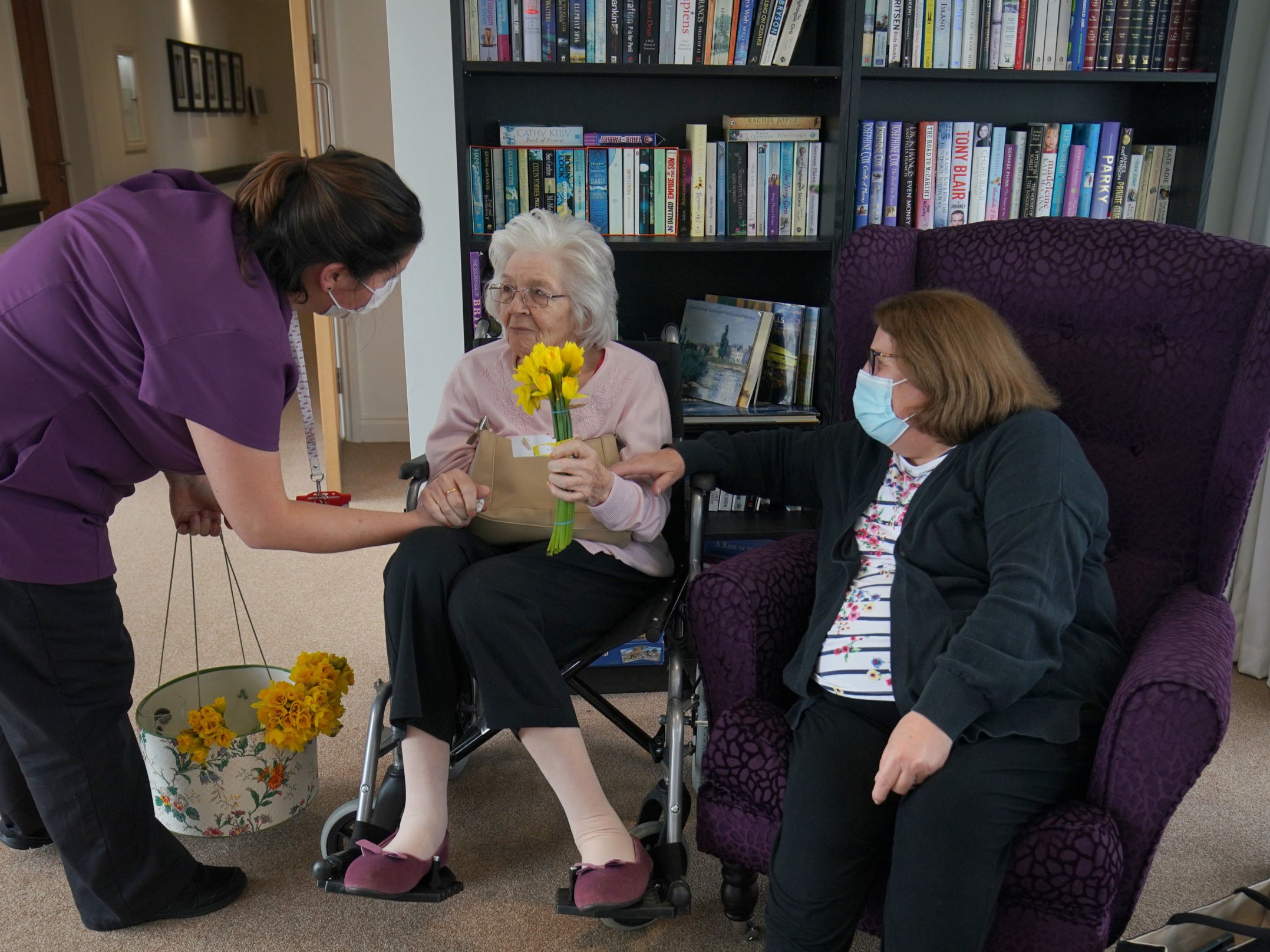 A member of staff gives a bunch of daffodils to Sylvia Newsom (centre) and her daughter Kay Fossett (right), who haven't seen each other since December, enjoy their first visit following the easing of rules at Gracewell of Sutton care home in South London