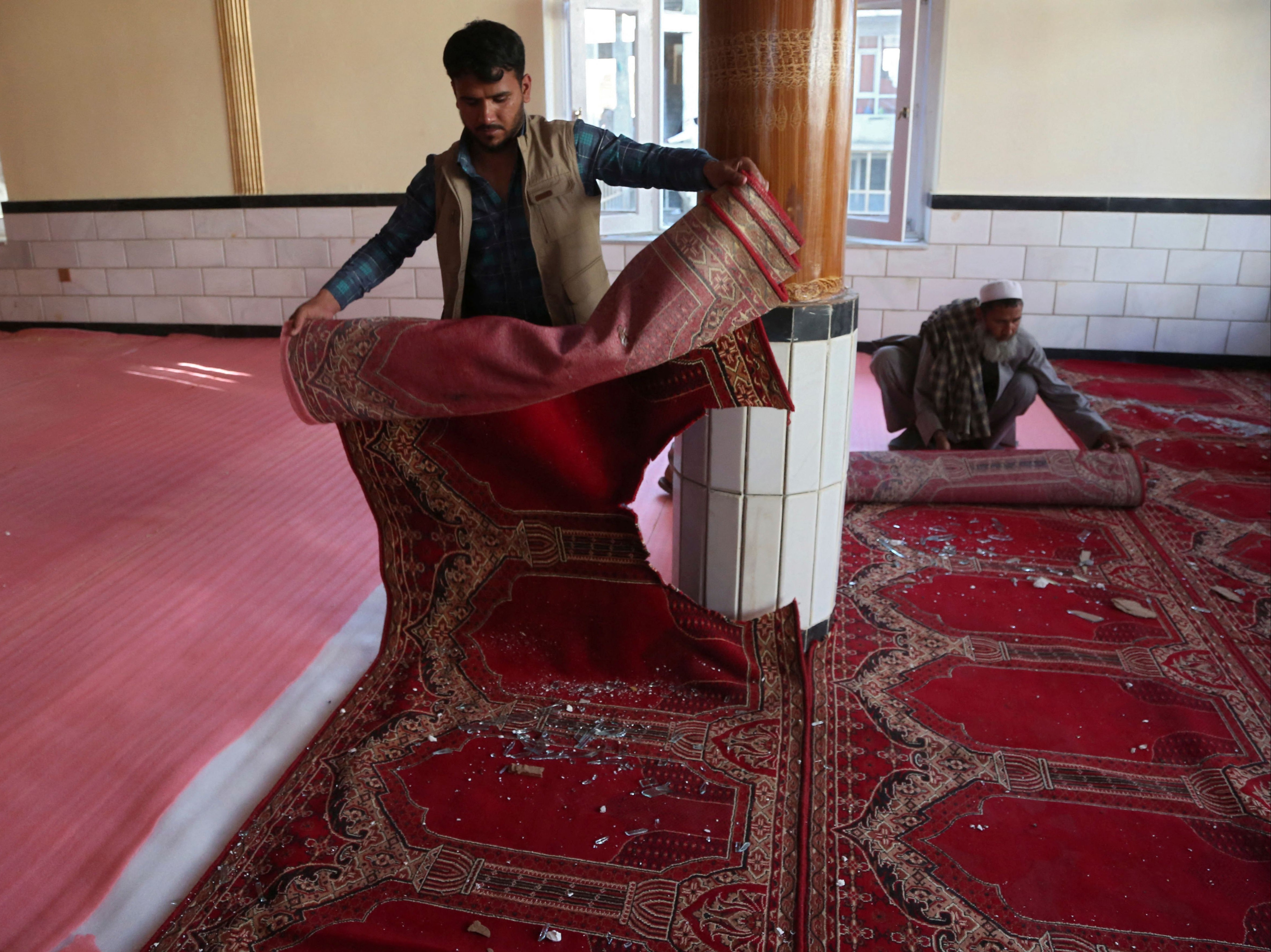 Devotees remove carpets from a mosque after a bomb blast on the outskirts of Kabul on Friday, which killed at least 12 people