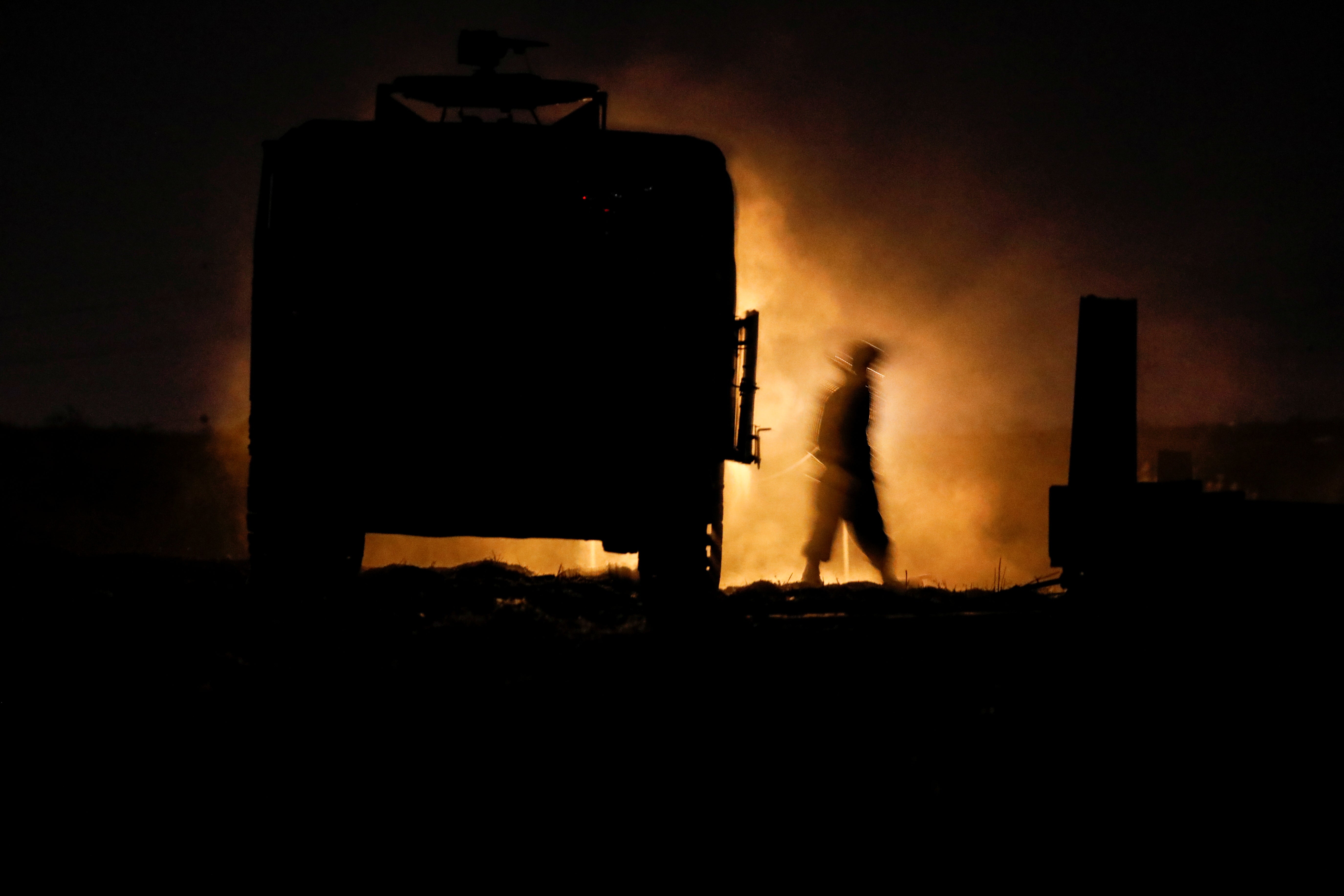 An Israeli soldier walks next to a military vehicle at a mobile artillery unit location on the Israeli side of the border with Gaza