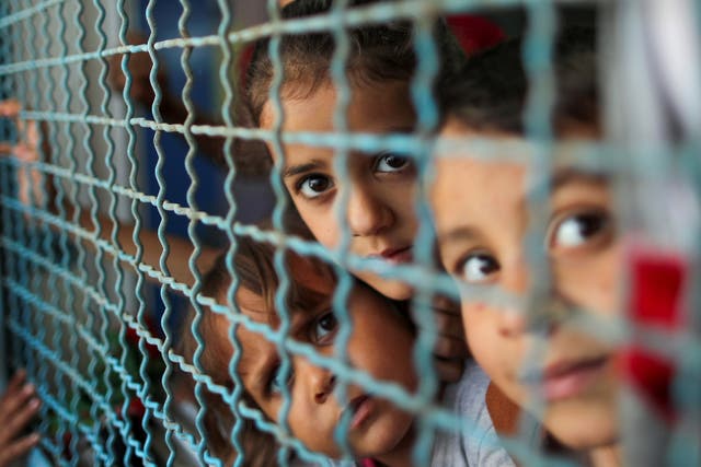 Palestinian children, who fled their homes due to Israeli air and artillery strikes, look through a window fence at a United Nations-run school where they take refuge, in Gaza City