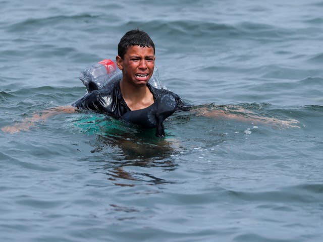 A boy cries as he swims using bottles as a float near the fence between the Spanish-Moroccan border