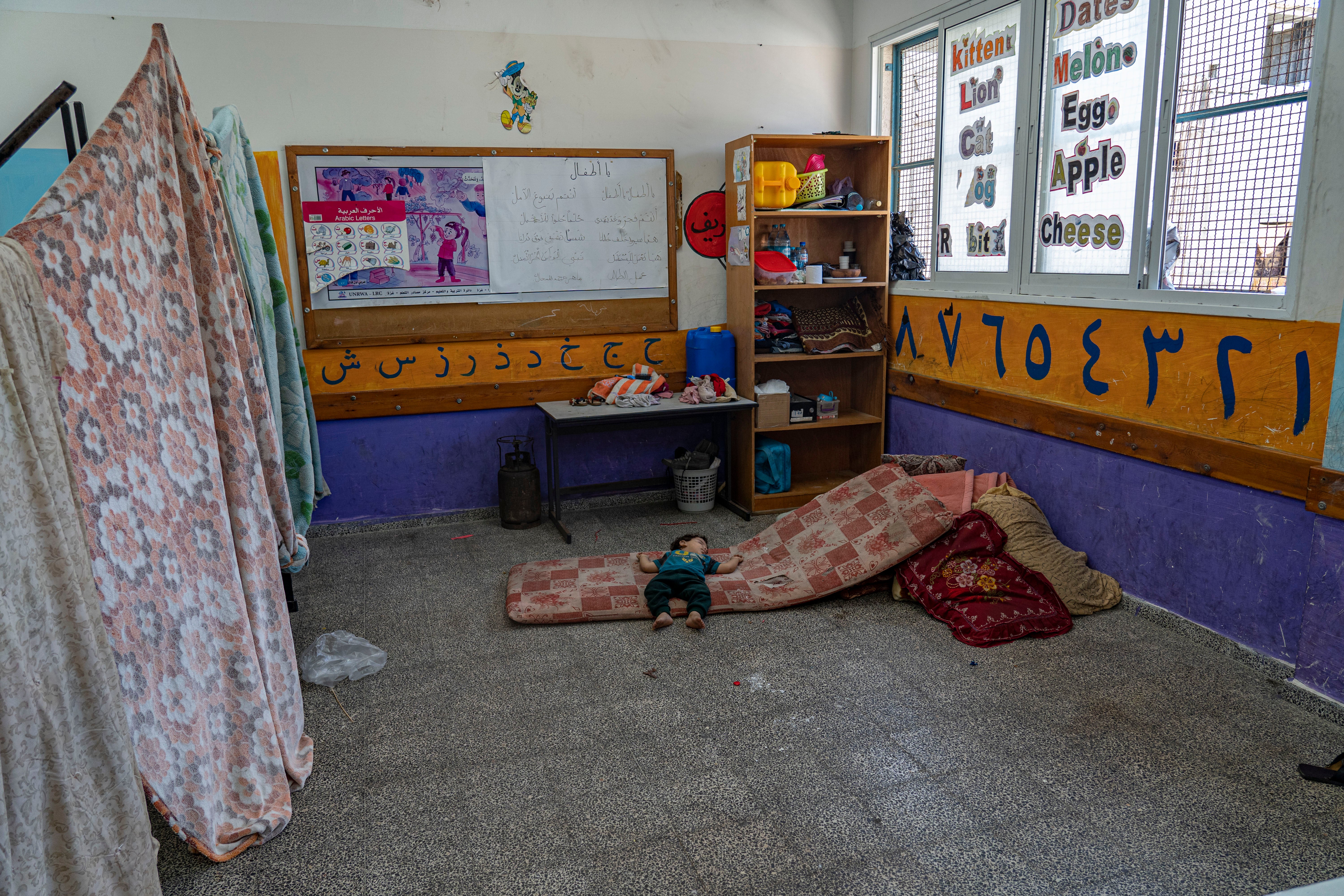 A baby lies on a foam mattress in a makeshift bedroom in a UNRWA school shelter