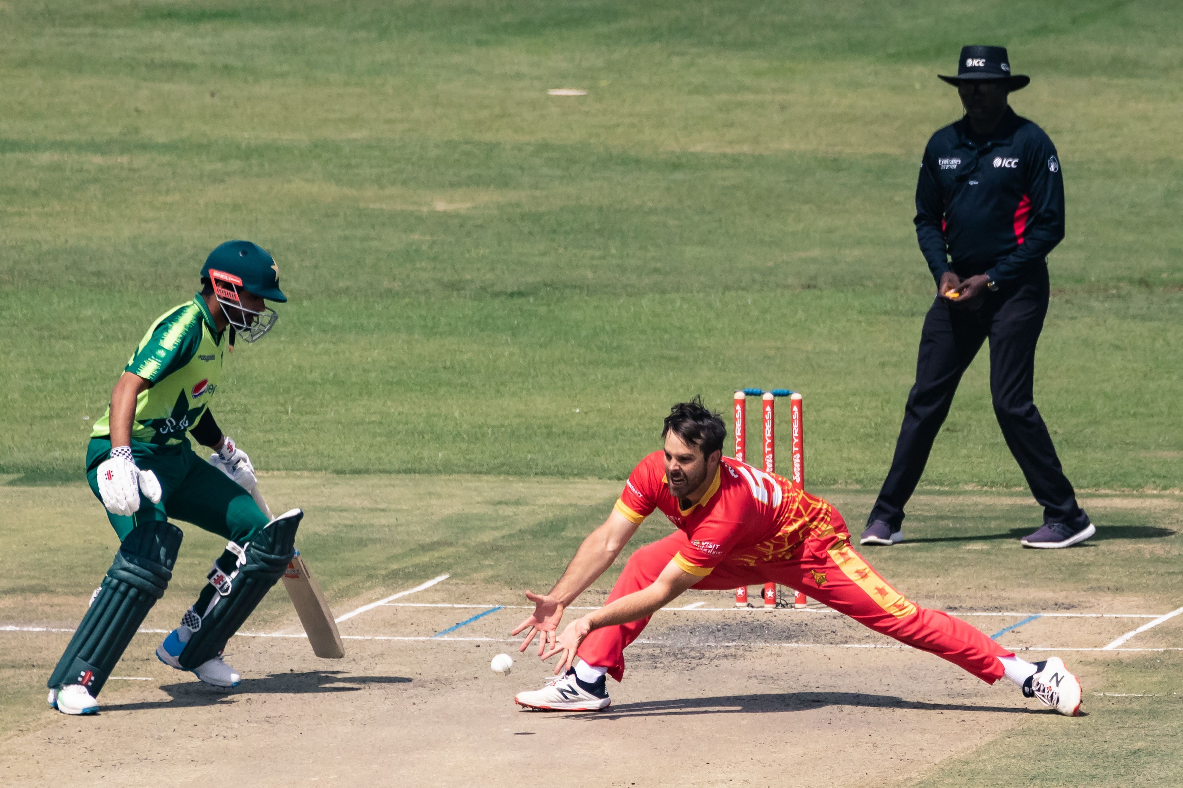 Zimbabwe’s Ryan Burl fields off his own bowling as Babar Azam and umpire Langton Rusere looks on during the third Twenty20 match