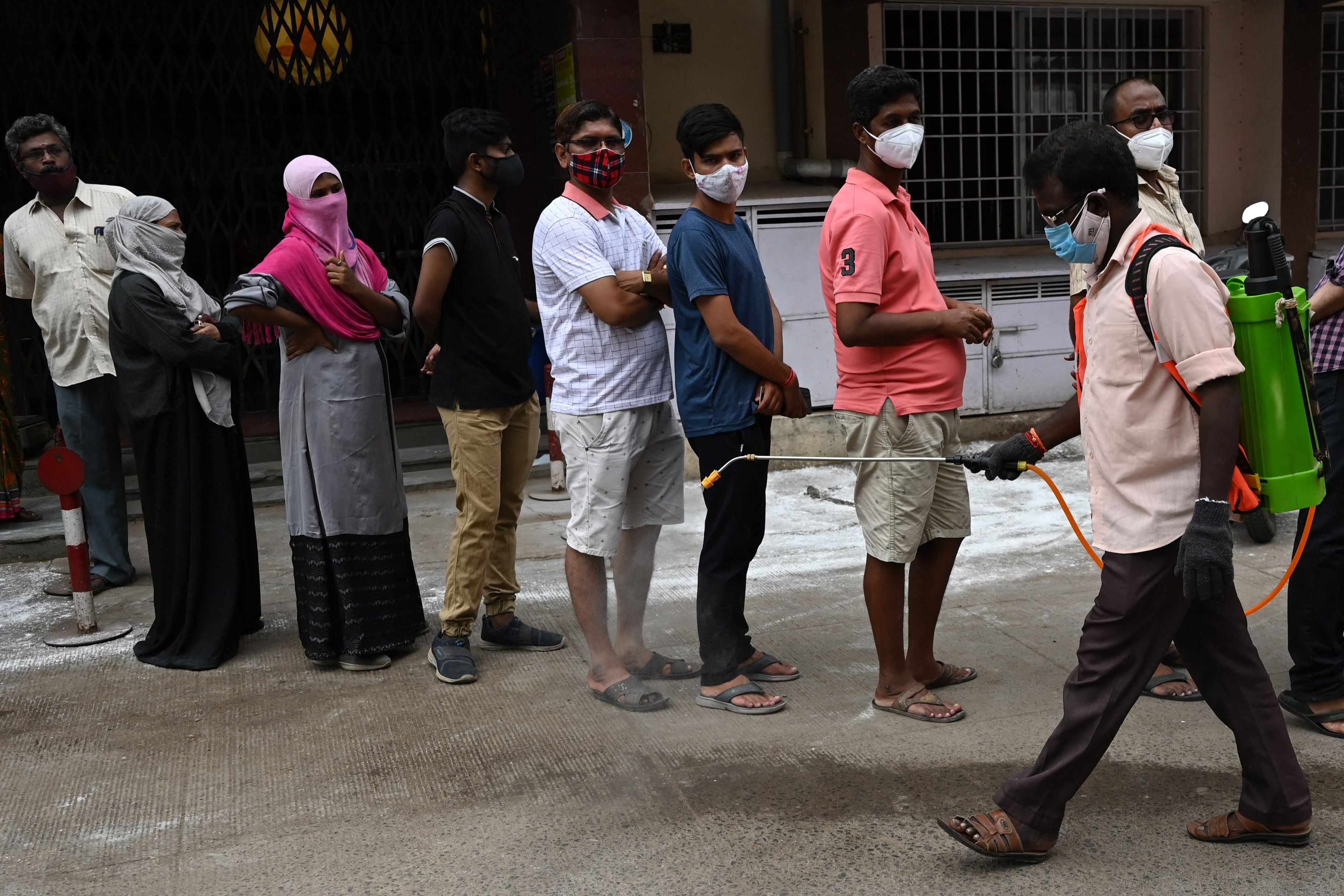 A health worker sanitises as people wait to get themselves inoculated with the dose of Covishield Covid-19 coronavirus vaccine at a vaccination camp in a residential area in Chennai on May 24, 2021. (Photo by Arun SANKAR / AFP) (Photo by ARUN SANKAR/AFP via Getty Images)