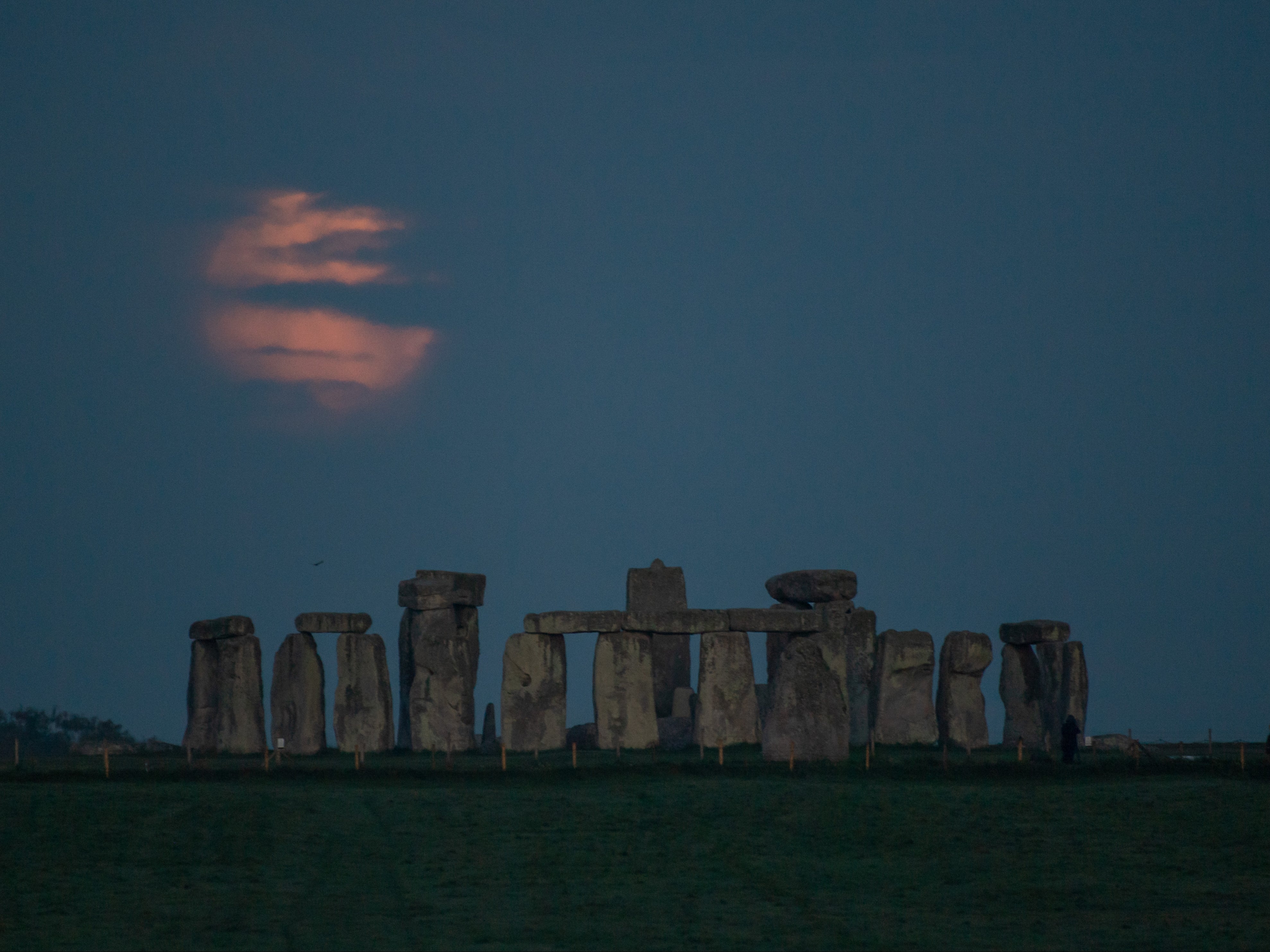 The moon, partially obscured by cloud, cuts a ghostly presence sets over Stonehenge in Wiltshire in the early hours of Wednesday 26 May 2021