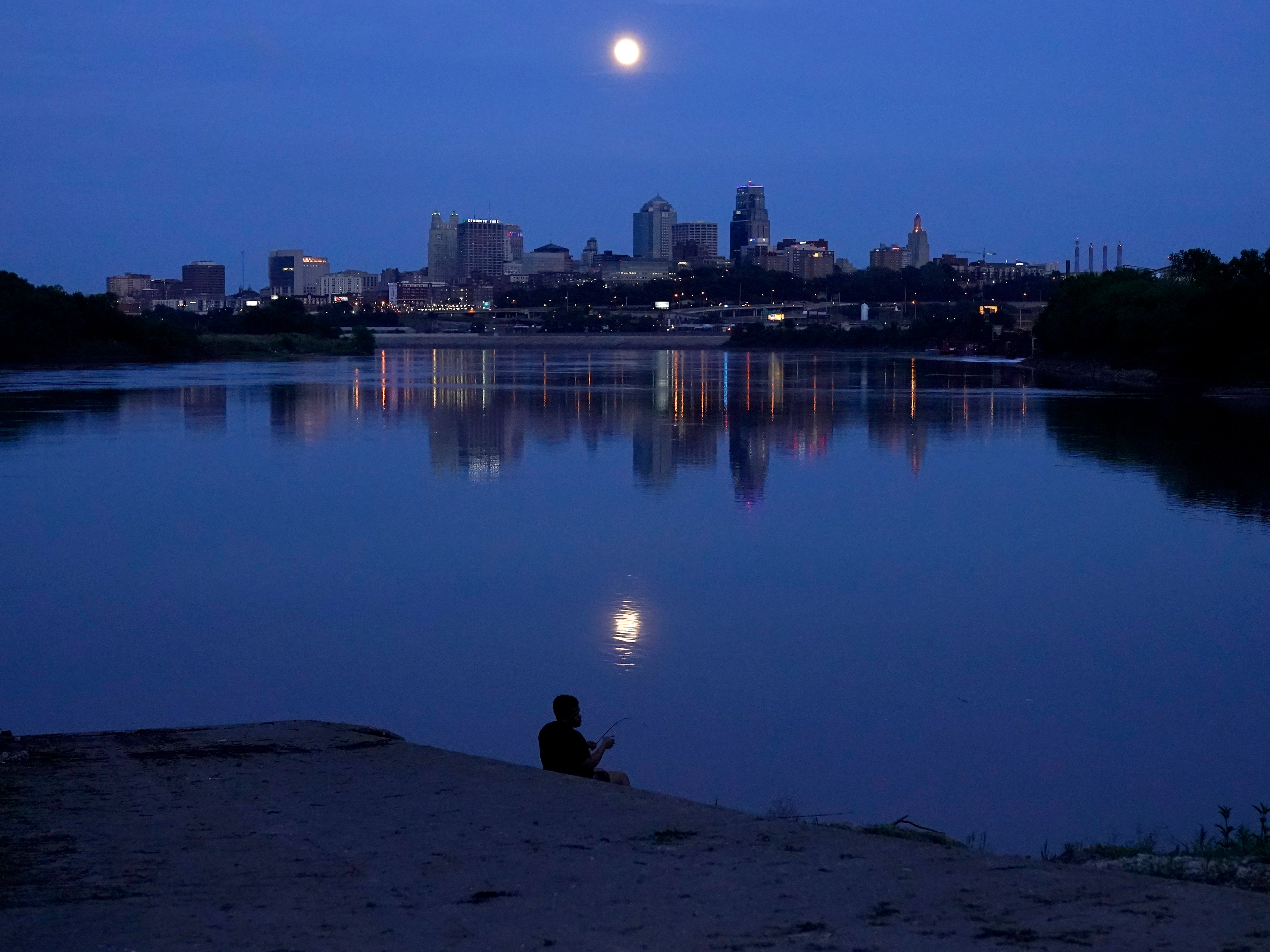 A man fishes in the Missouri River as the full moon rises beyond the skyline of downtown Kansas City, Missouri, on Tuesday 25 May 2021