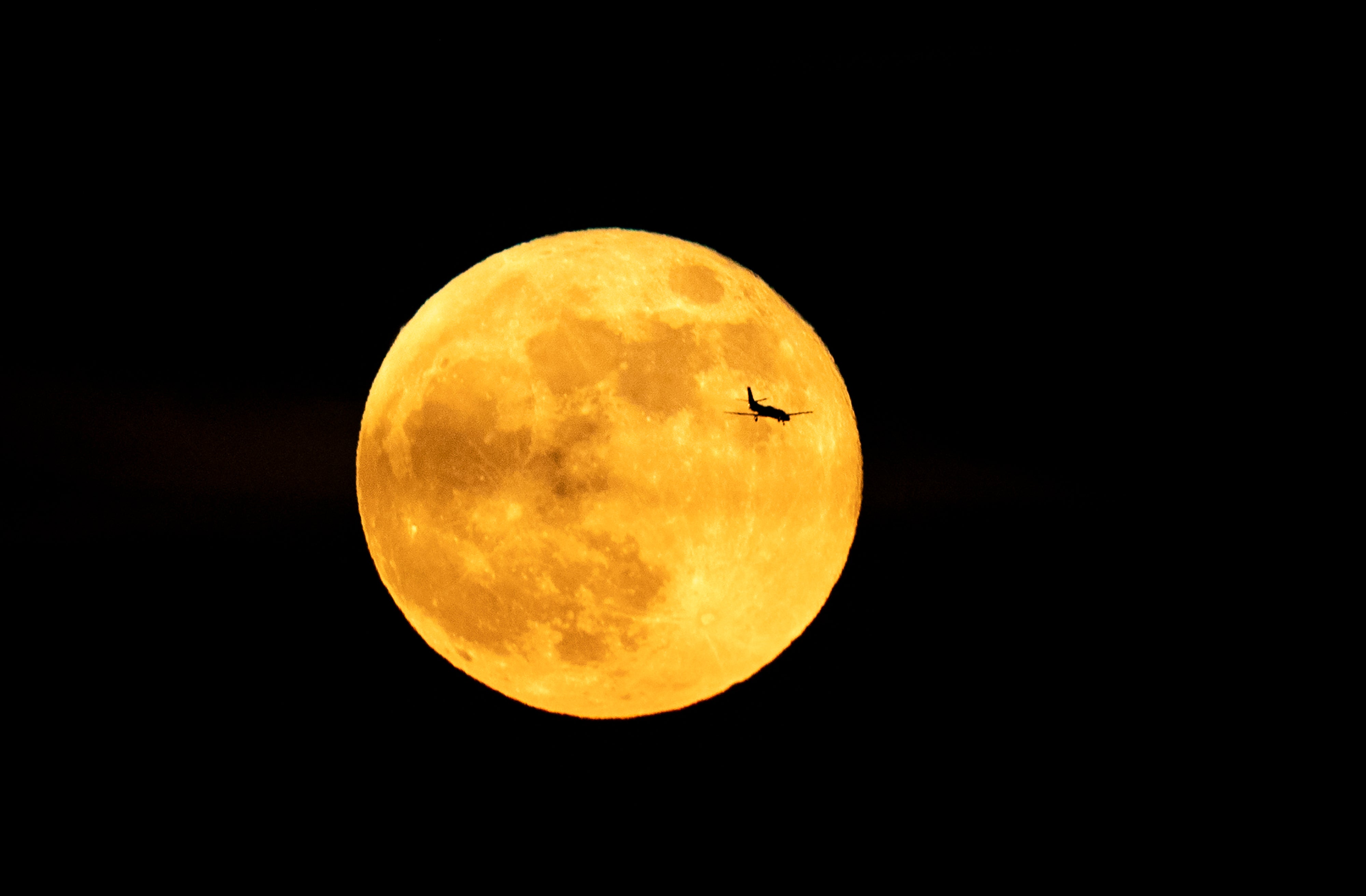 The silhouette of a plane is seen in front of the full moon on May 26, 2021 in Rome
