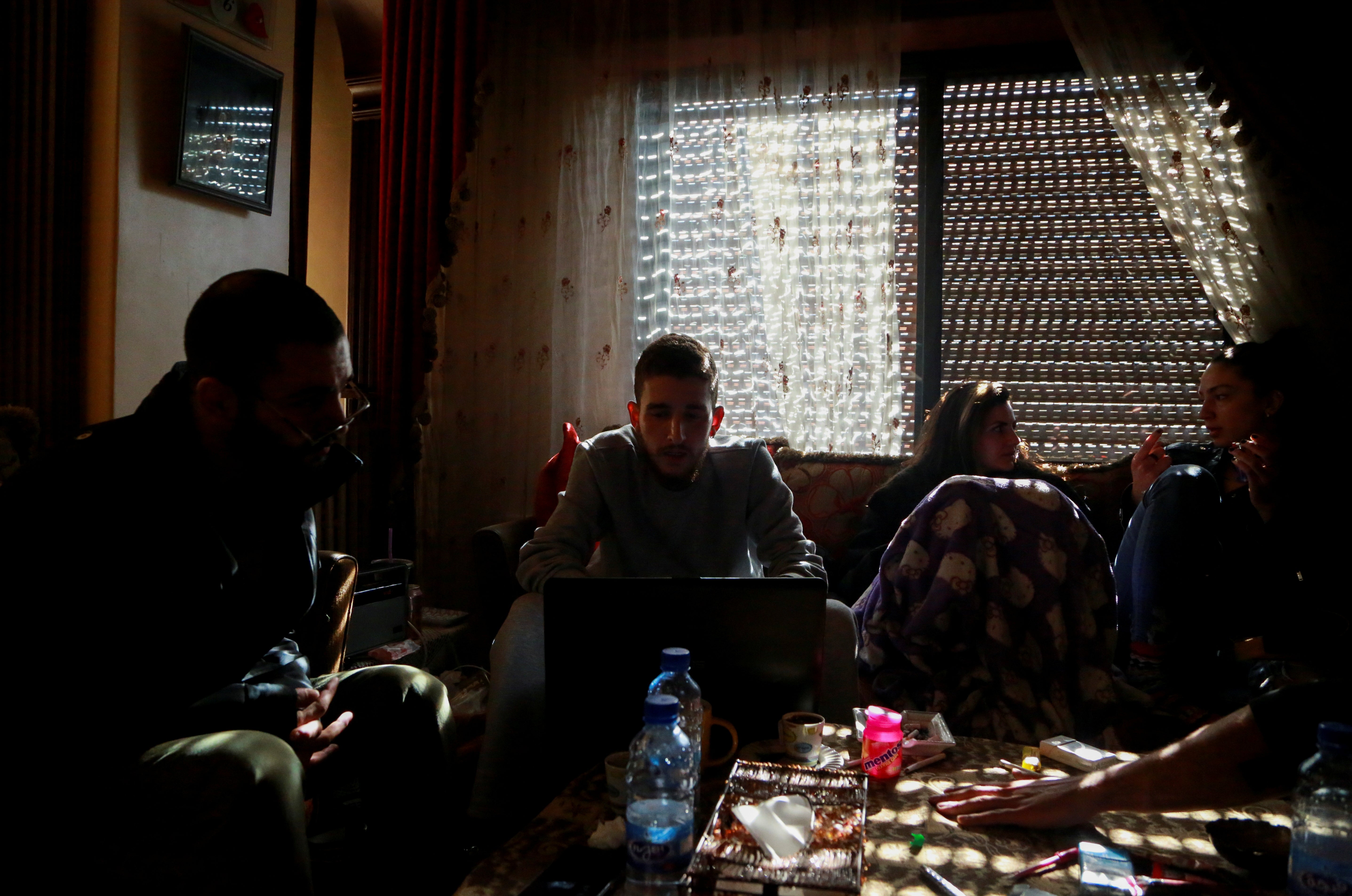 Jawad works on his laptop as he sits with his friends at his home