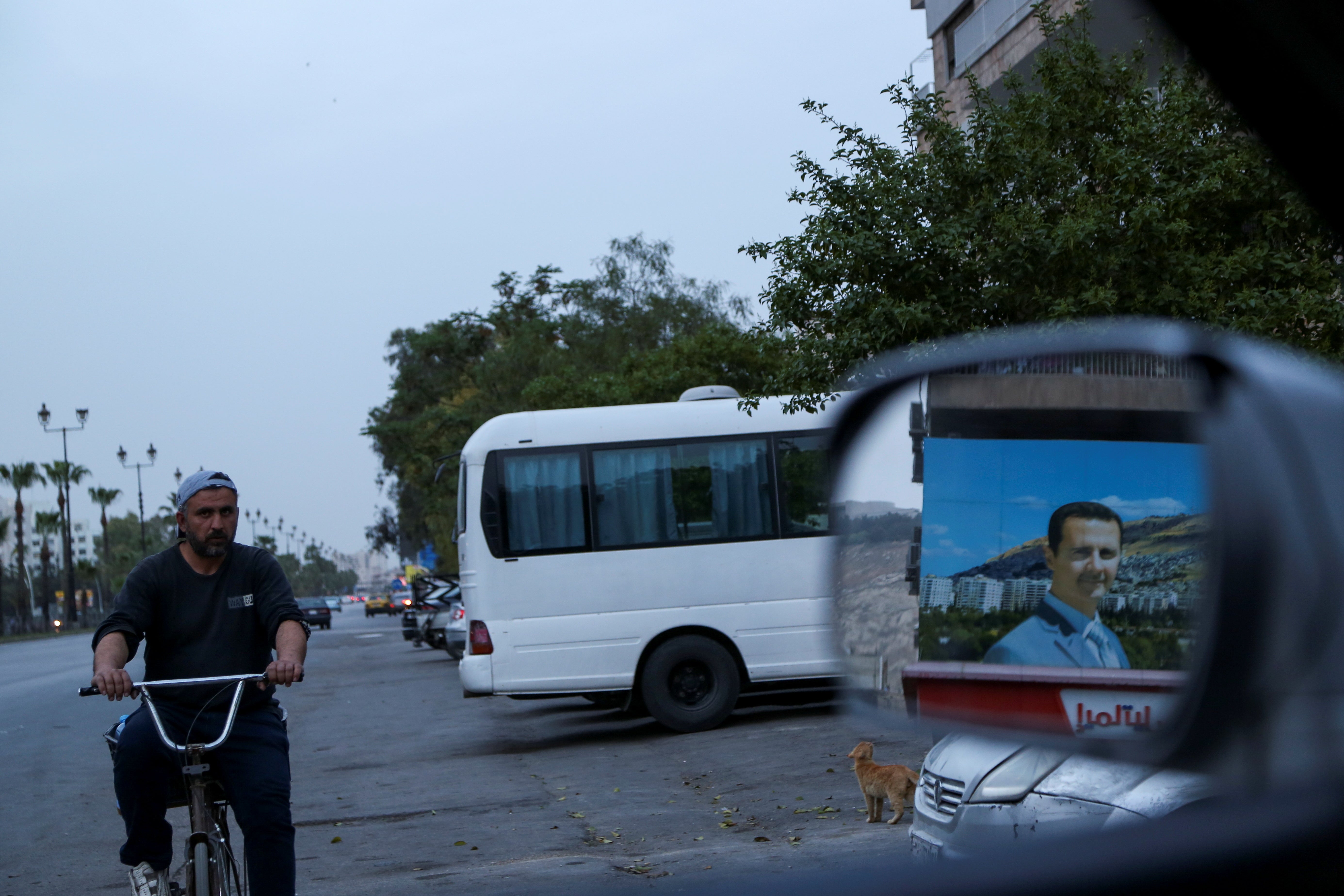 A picture of Syrian president Bashar al-Assad is reflected in a mirror, as a man cycles along a highway in Damascus